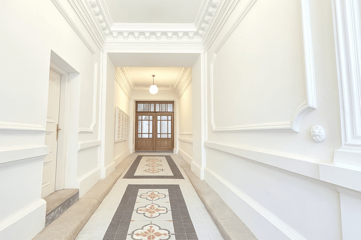 Langer, heller Flur im Altbau mit Stuckelementen, gemustertem Fliesenboden und Holztüren.