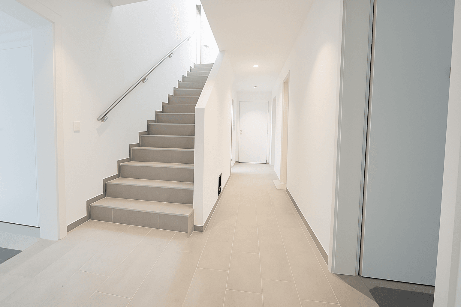 Moderner Flur mit Treppe, Fliesenboden und schlichten weißen Wänden.