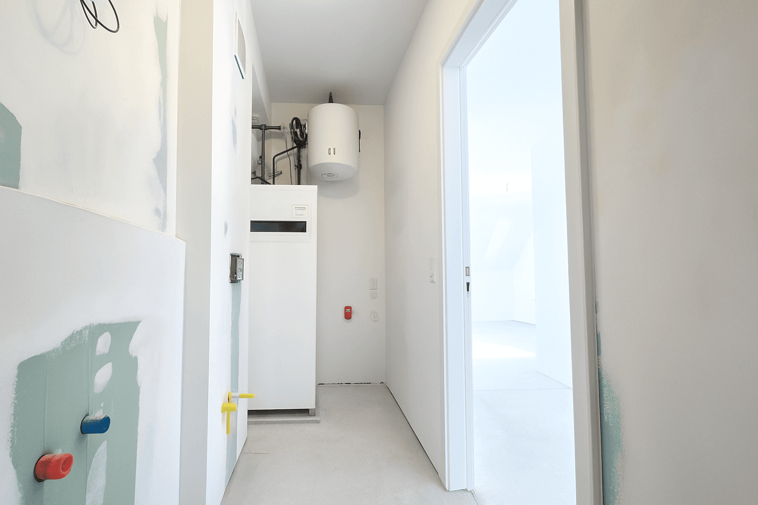 Technikraum mit Warmwasserboiler und Heizungsinstallationen, noch im Bauzustand.