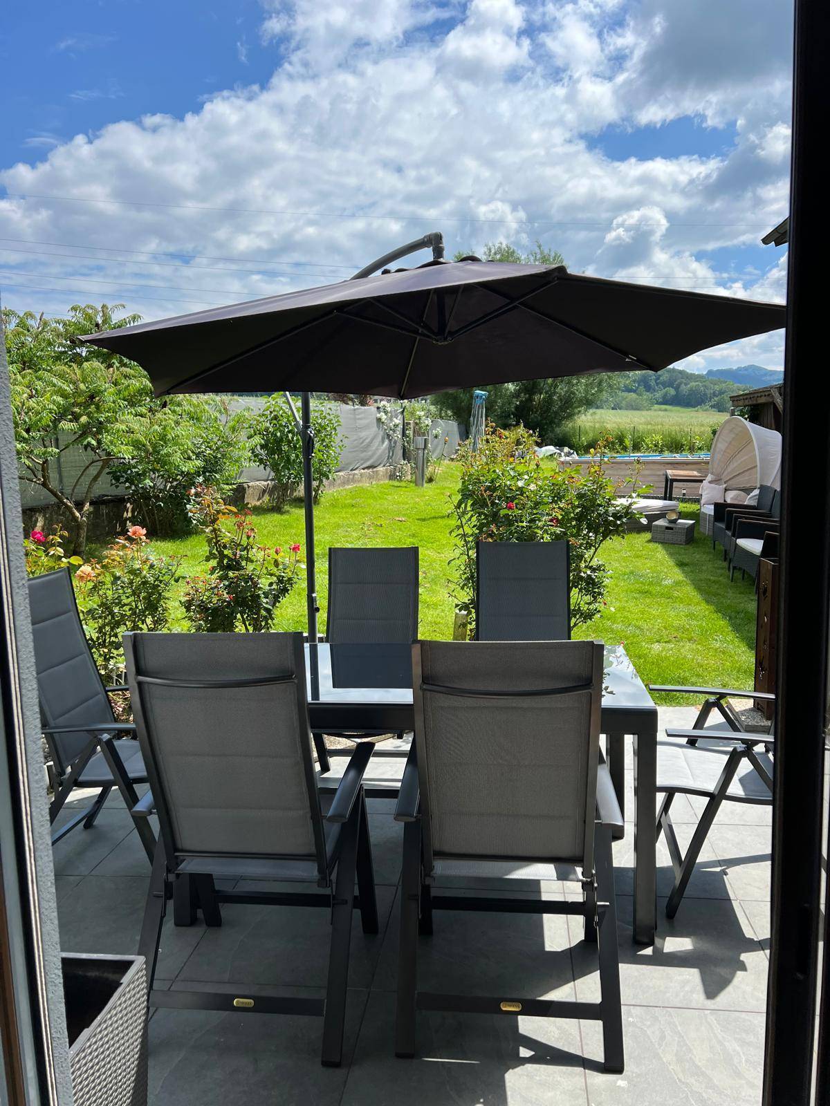 Gepflegter Gartenbereich mit Rasenfläche, Outdoor-Sitzgruppe und Sonnenschirm an einem sonnigen Tag.