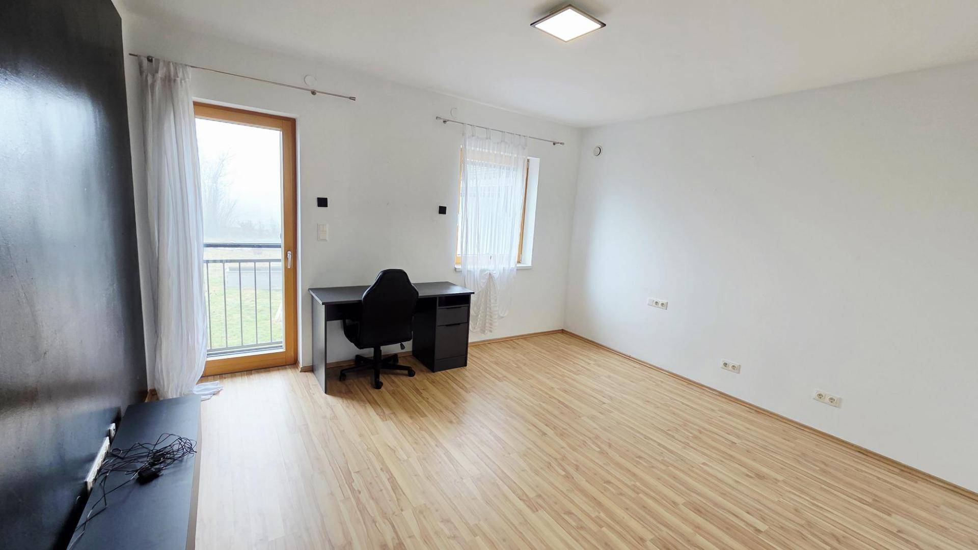 Helles Zimmer mit Laminatboden, Schreibtisch und Zugang zu einem französischen Balkon.