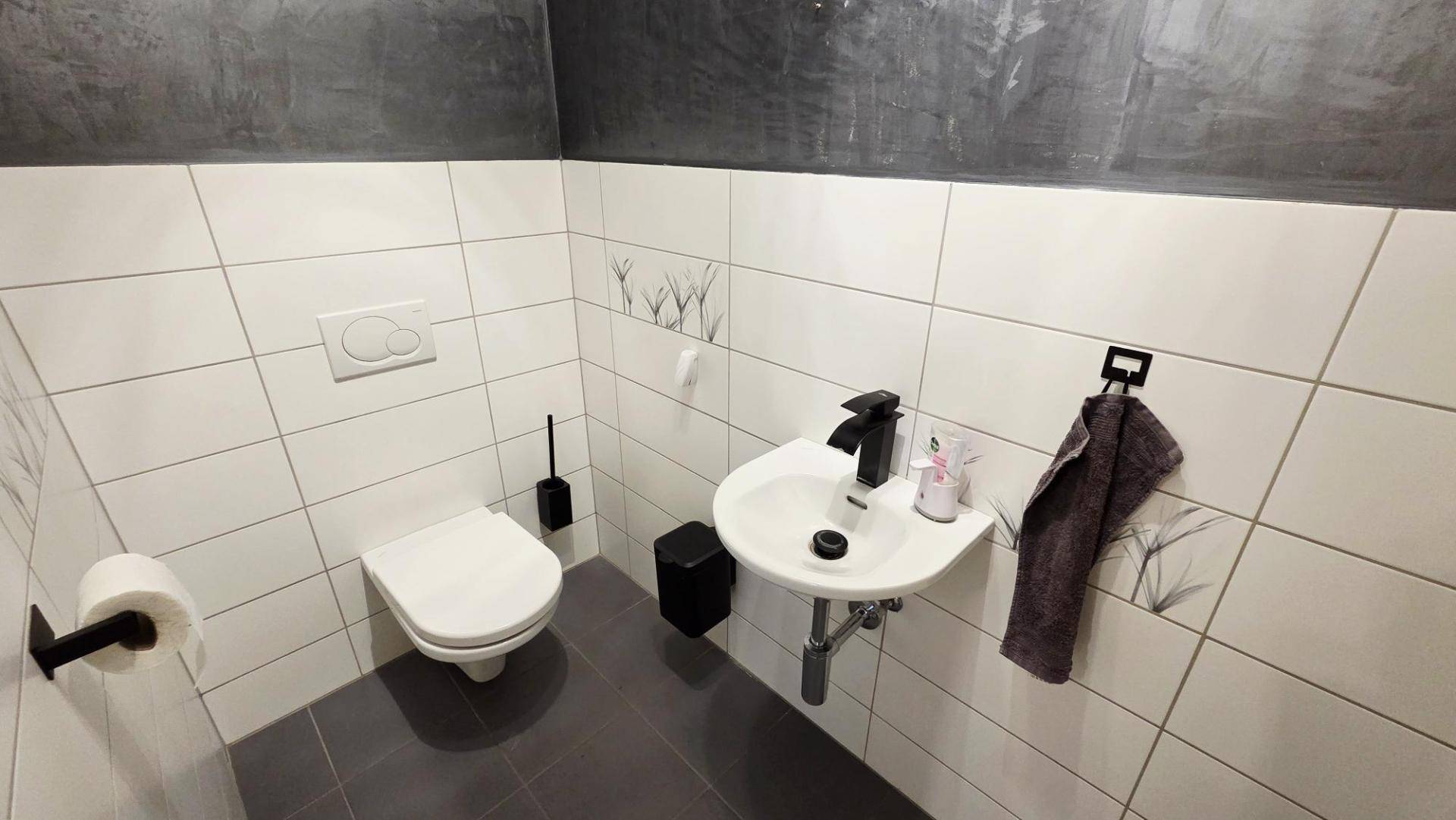 Modernes Gäste-WC mit Wand-WC, kleinem Waschbecken und Fliesen an Wänden und Boden.