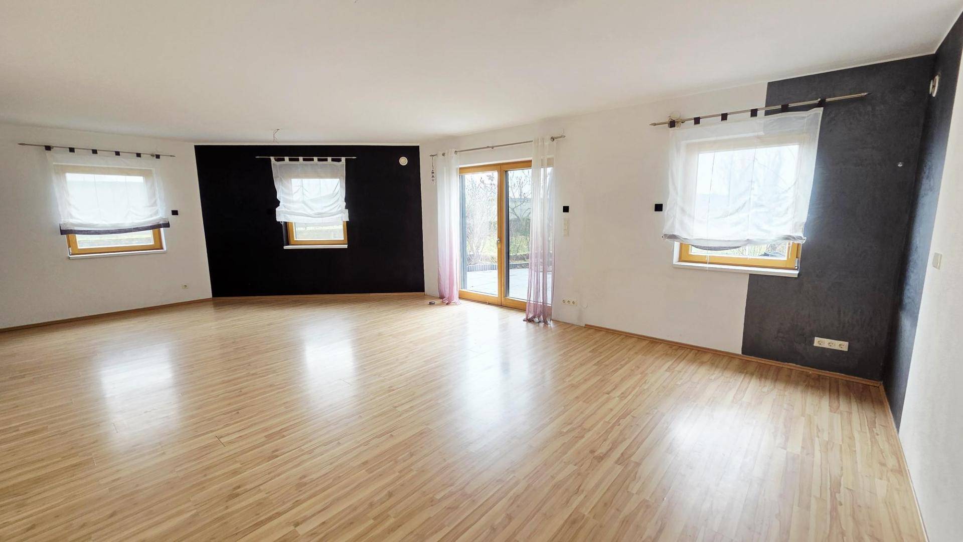 Geräumiger Wohnbereich mit Laminatboden, hellen Wänden und Zugang zur Terrasse.