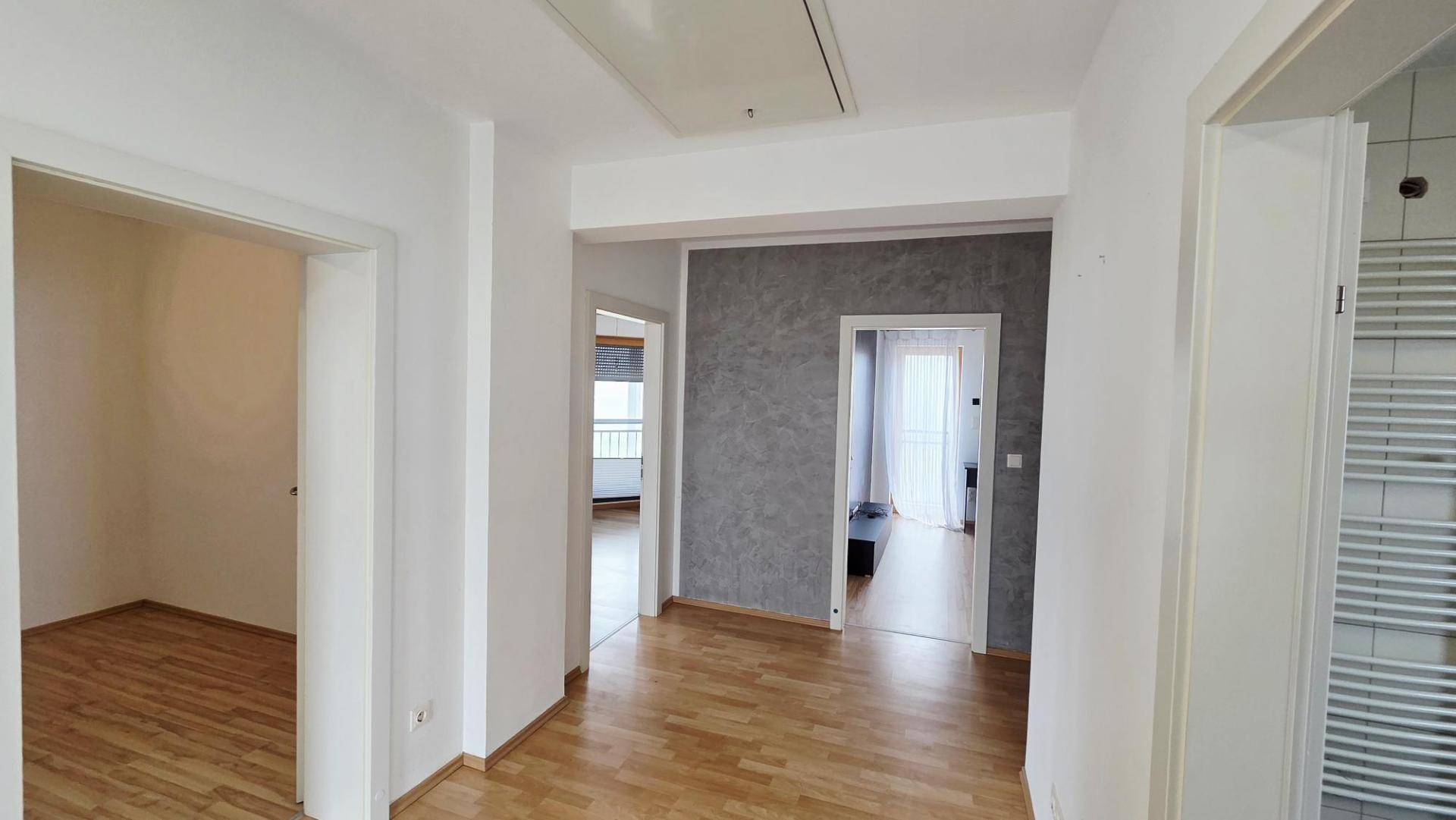 Heller Flur mit Laminatboden, weißen Wänden und Zugang zu mehreren Zimmern.