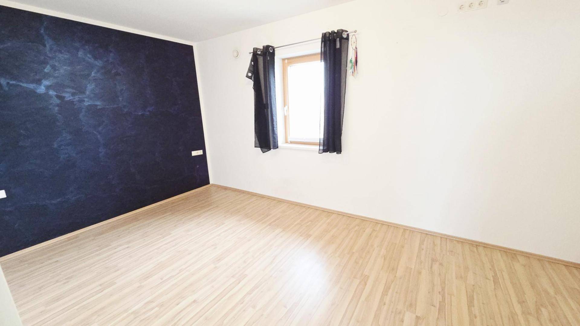 Schlafzimmer mit Laminatboden, einer dunklen Akzentwand und Fenster mit Vorhängen.