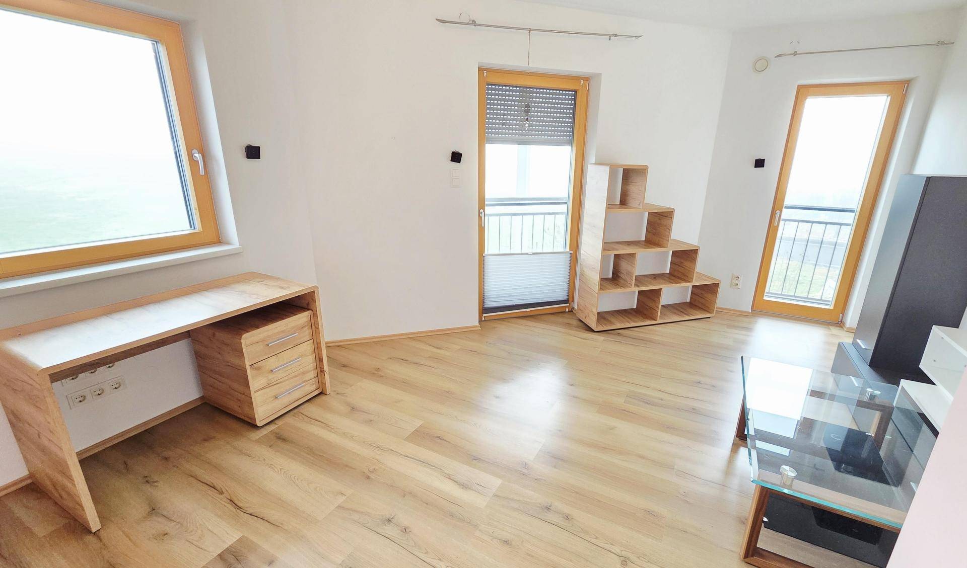 Helles Zimmer mit Laminatboden, Schreibtisch und zwei Fenstertüren mit französischem Balkon.