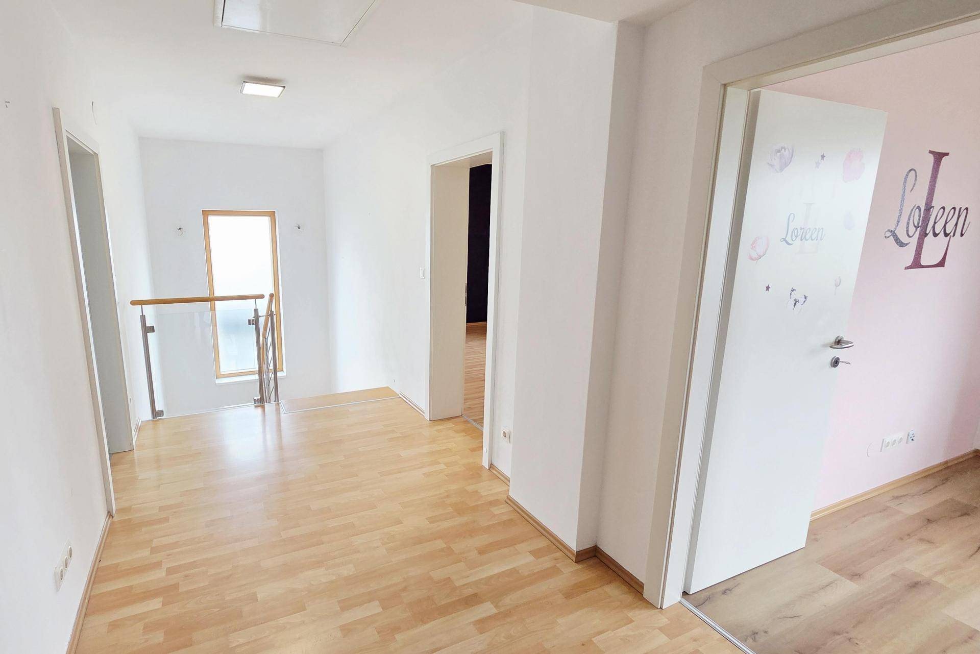 Heller Flur im Obergeschoss mit Laminatboden, Treppengeländer und Zugang zu Zimmern.