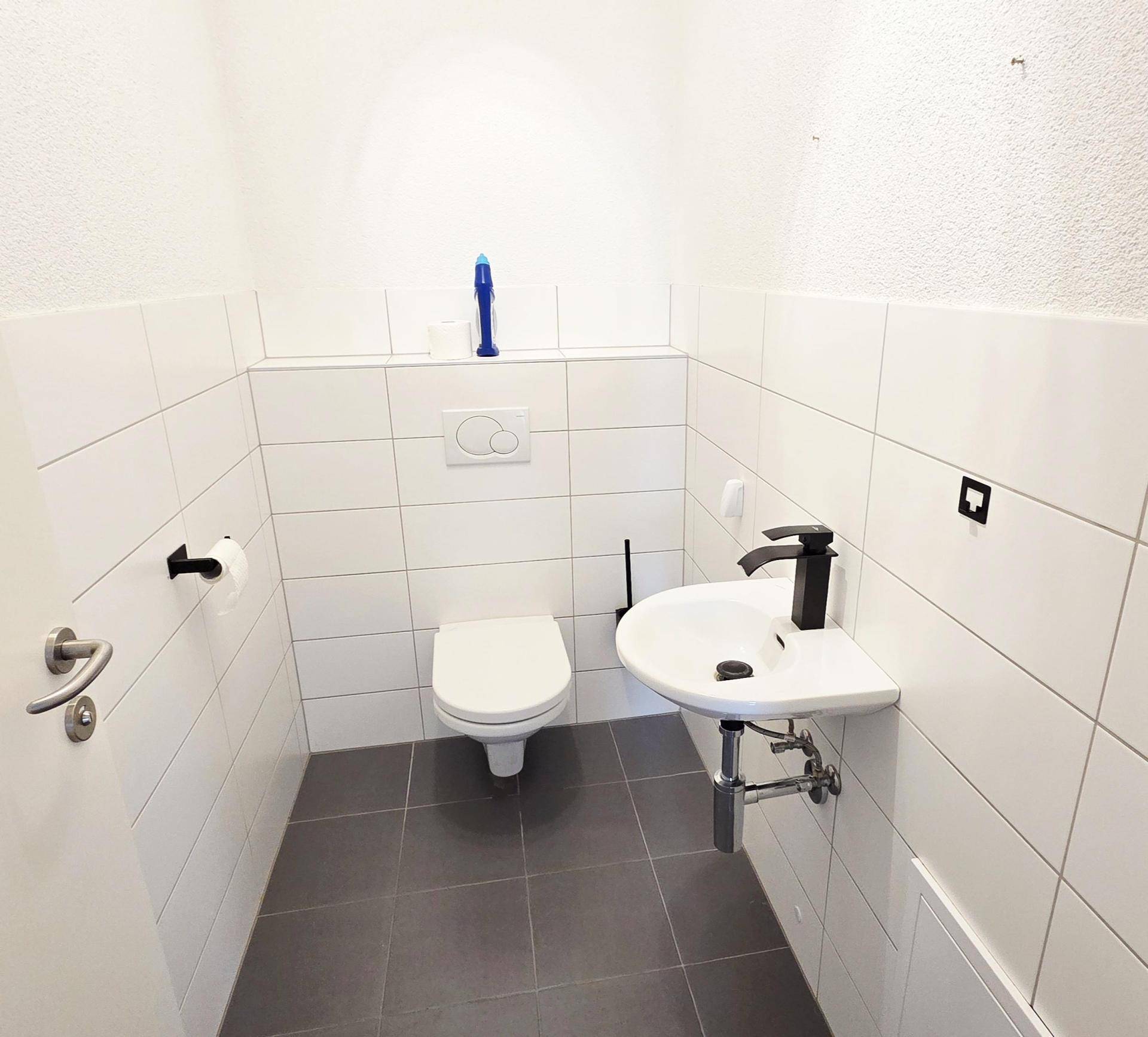 Kleines Gäste-WC mit weißen Fliesen, Wand-WC und modernem Waschbecken.