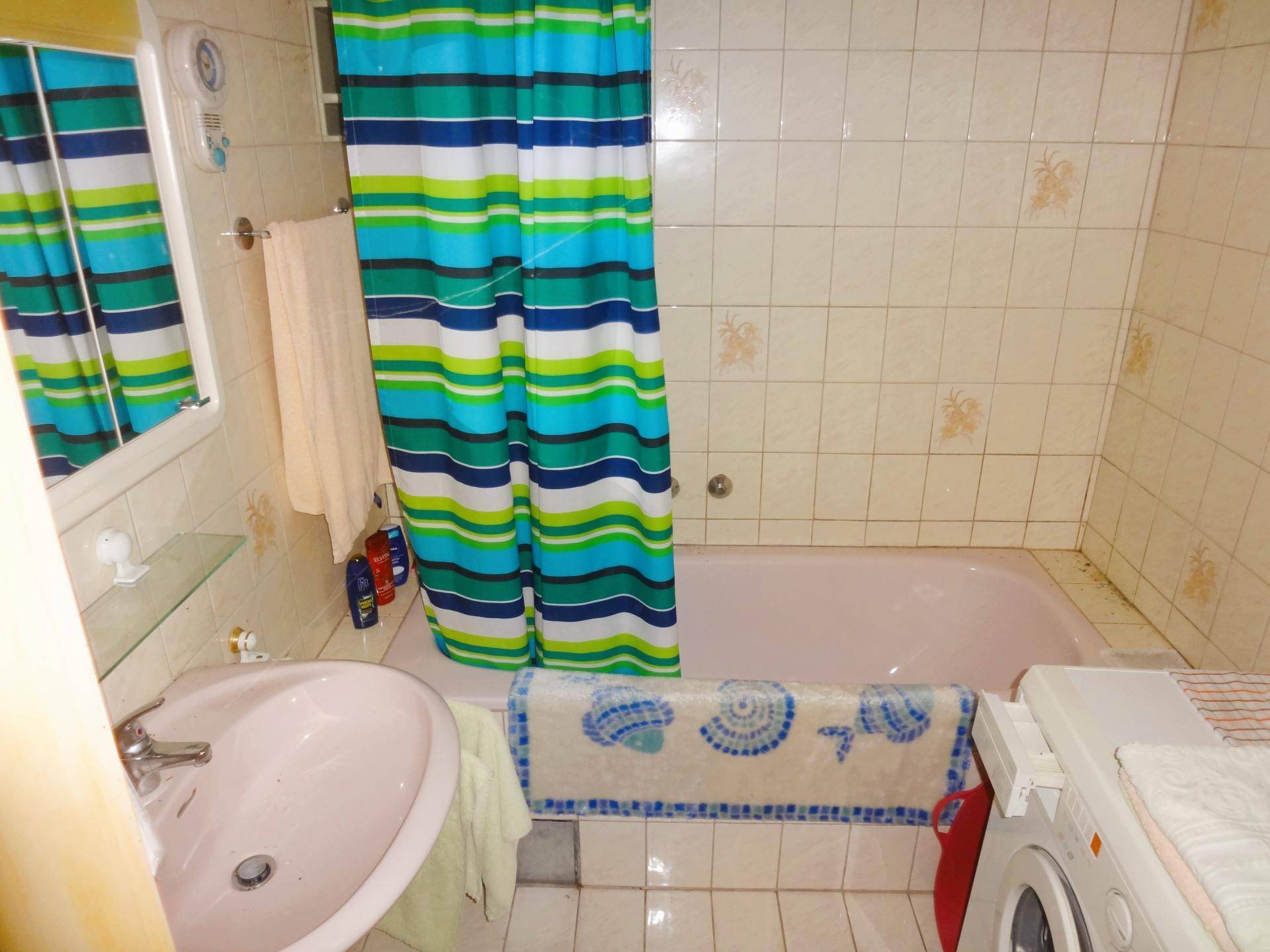 Badezimmer mit rosa Badewanne, Waschbecken und farbenfrohem Duschvorhang.