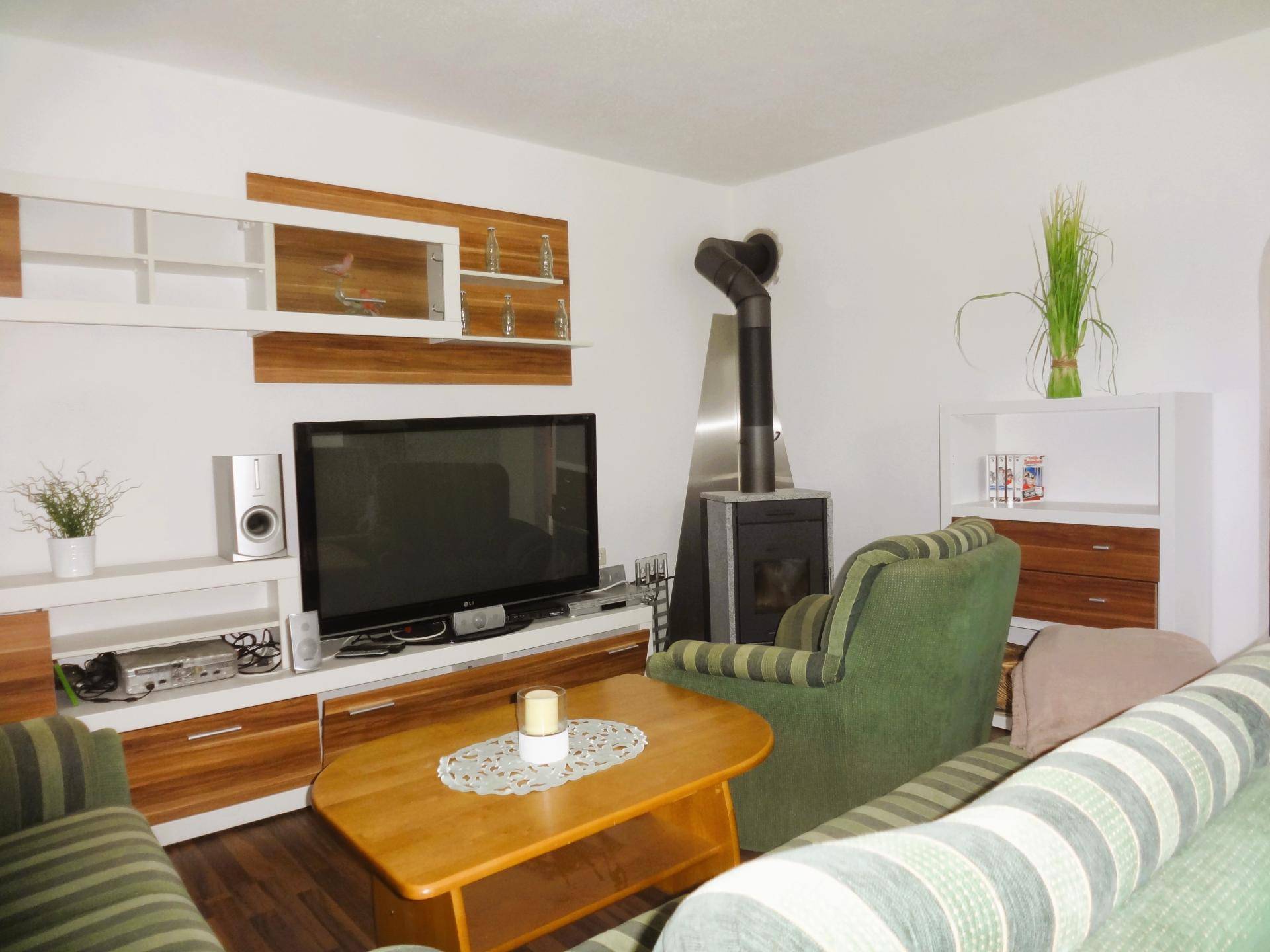 Wohnzimmer mit Holzofen, TV-Möbeln und gestreiften Sofas in grünen Farbtönen.