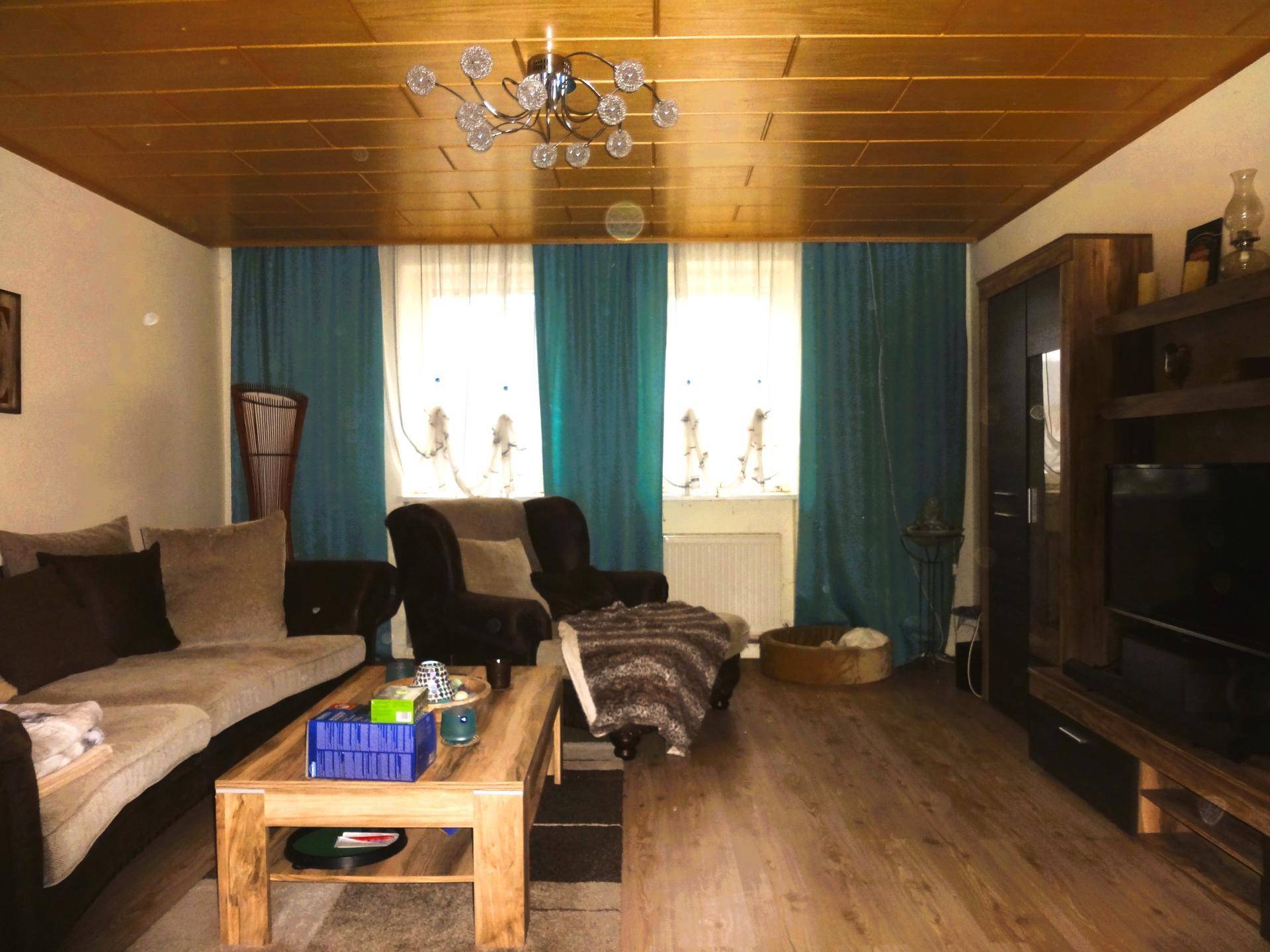 Gemütliches Wohnzimmer mit Holzdecke, Parkettboden und bequemen Sofas in warmen Farben.