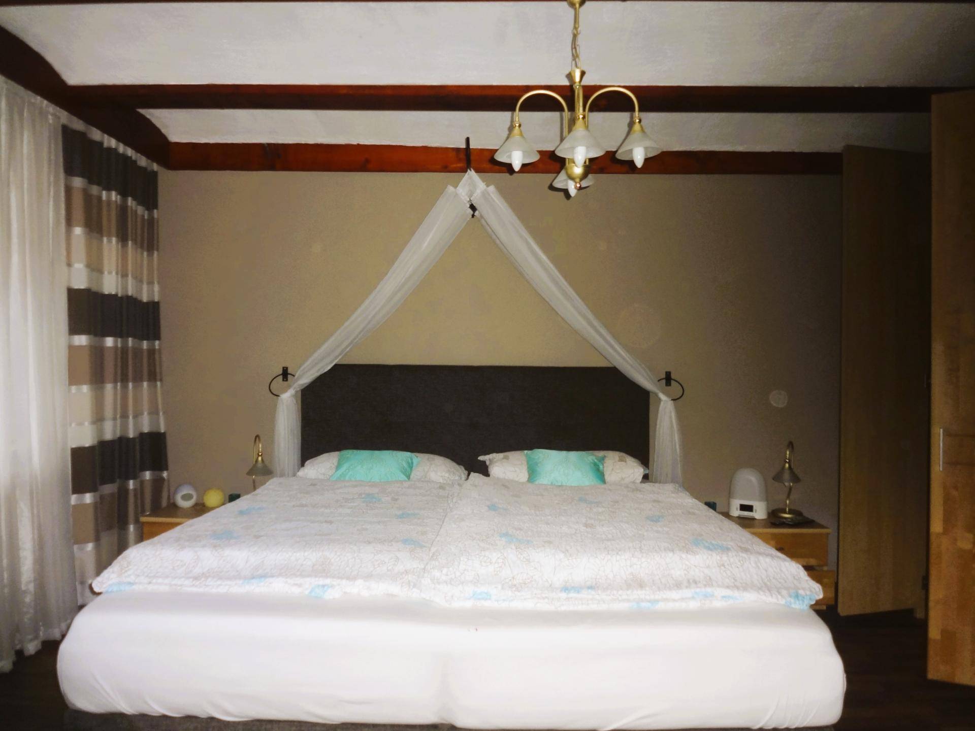 Schlafzimmer mit Doppelbett, Holzbalken an der Decke und traditioneller Beleuchtung.