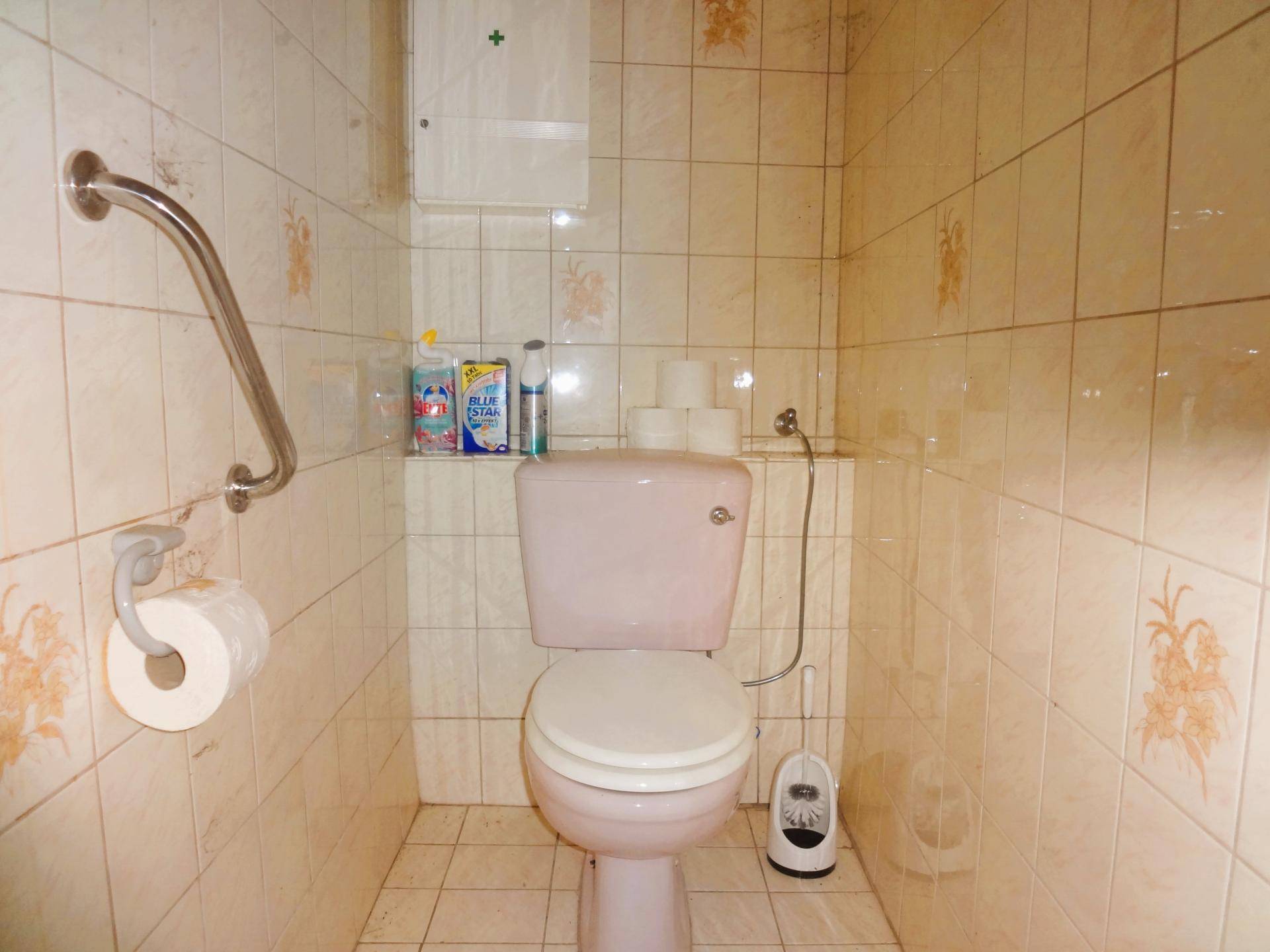 Separate Toilette mit beigefarbenen Fliesen, WC und Haltegriff an der Wand.