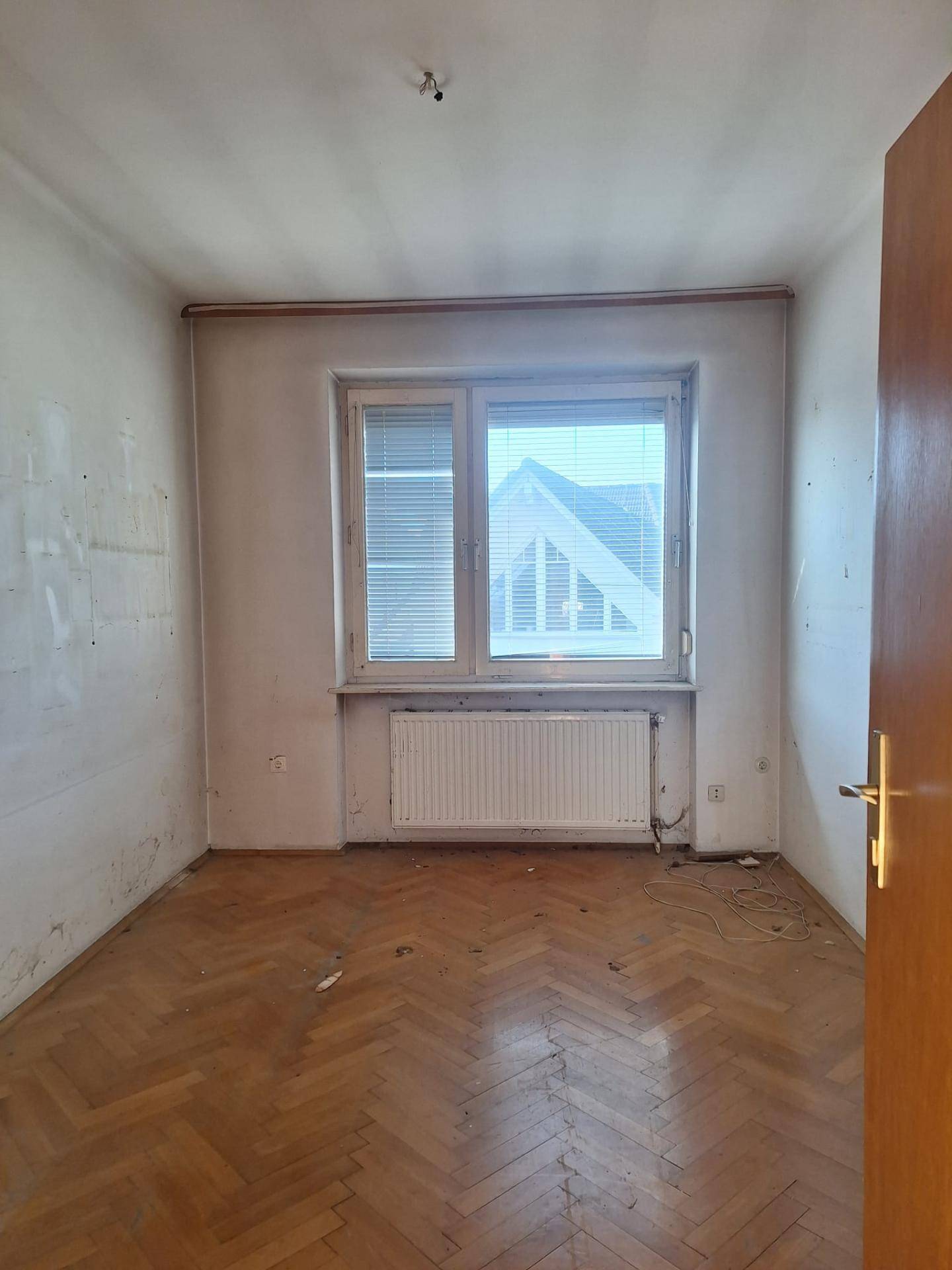 Leerer Raum mit Parkettboden, großem Fenster und Heizkörper, bereit für die Einrichtung.