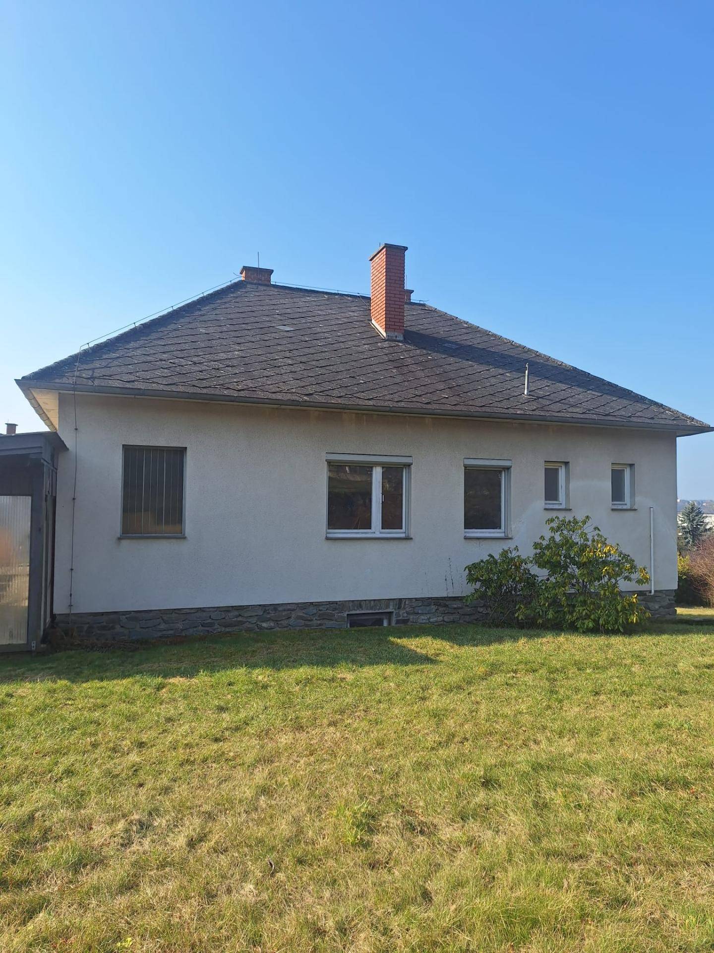 Rückansicht des Hauses mit Garten und überdachtem Anbau unter blauem Himmel.