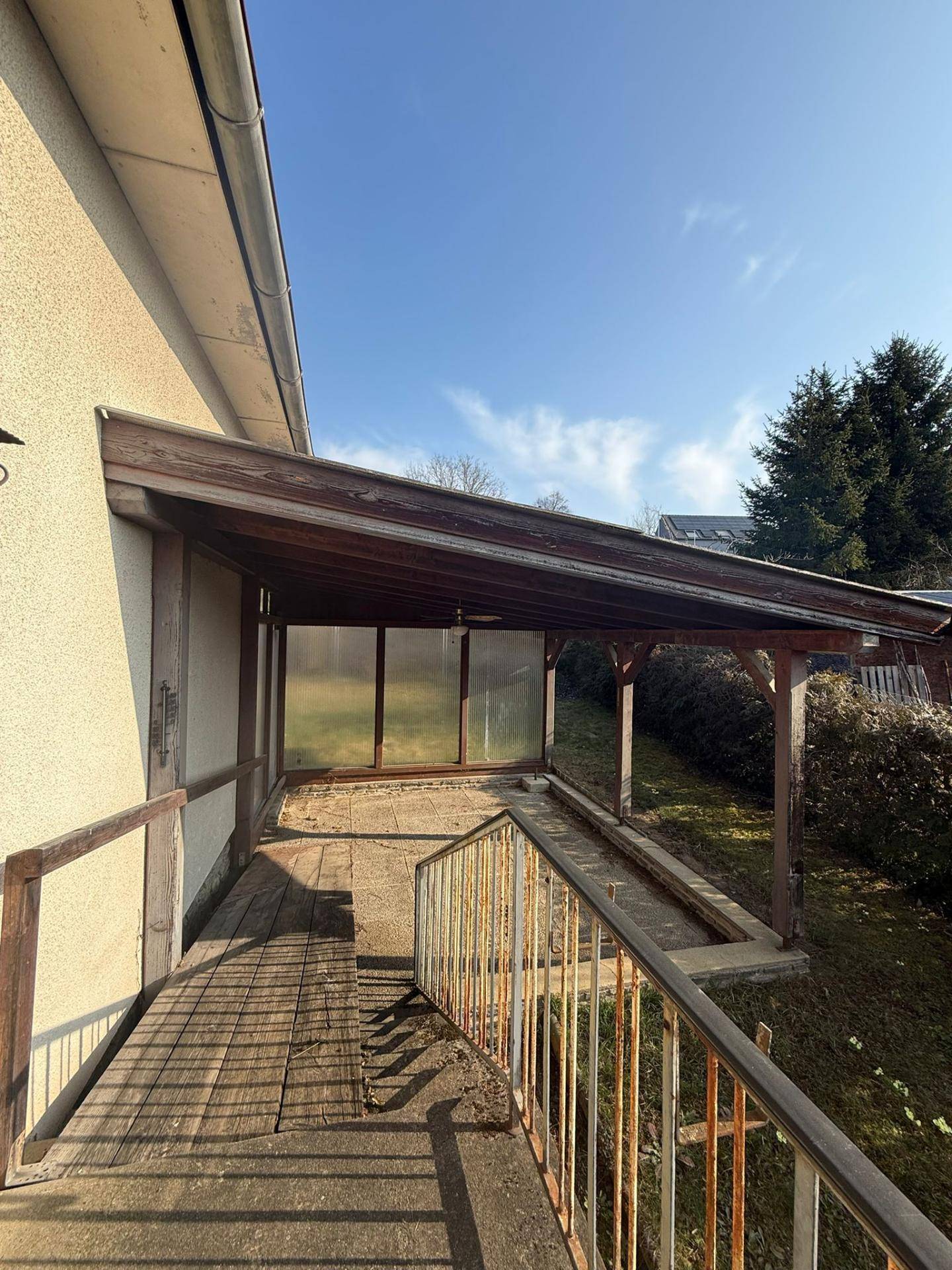 Überdachte Terrasse mit Holzkonstruktion und Geländer, die zum Garten führt.