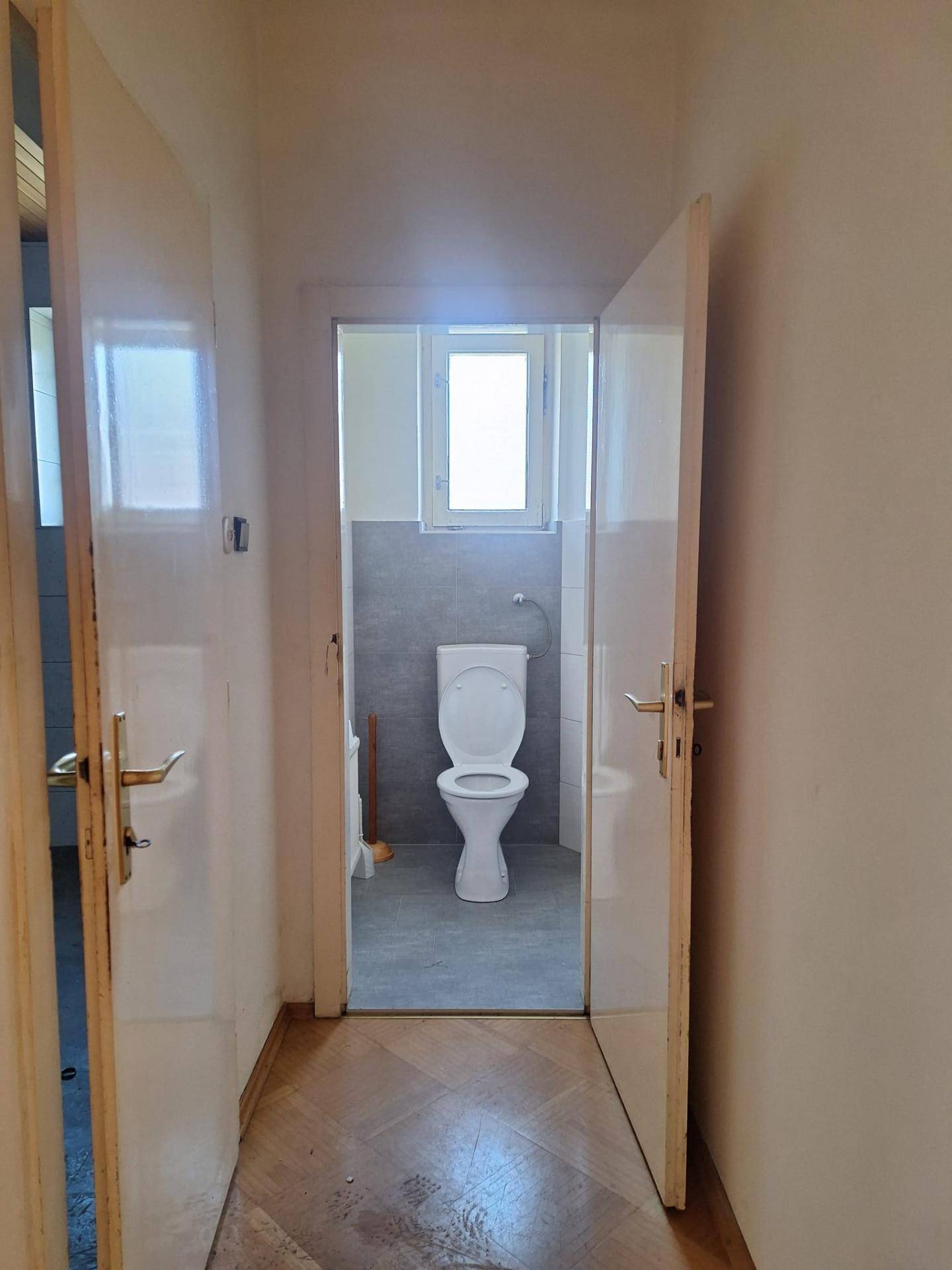 Kleines WC mit Toilette, Fliesenboden und Fenster, in gutem, funktionalem Zustand.
