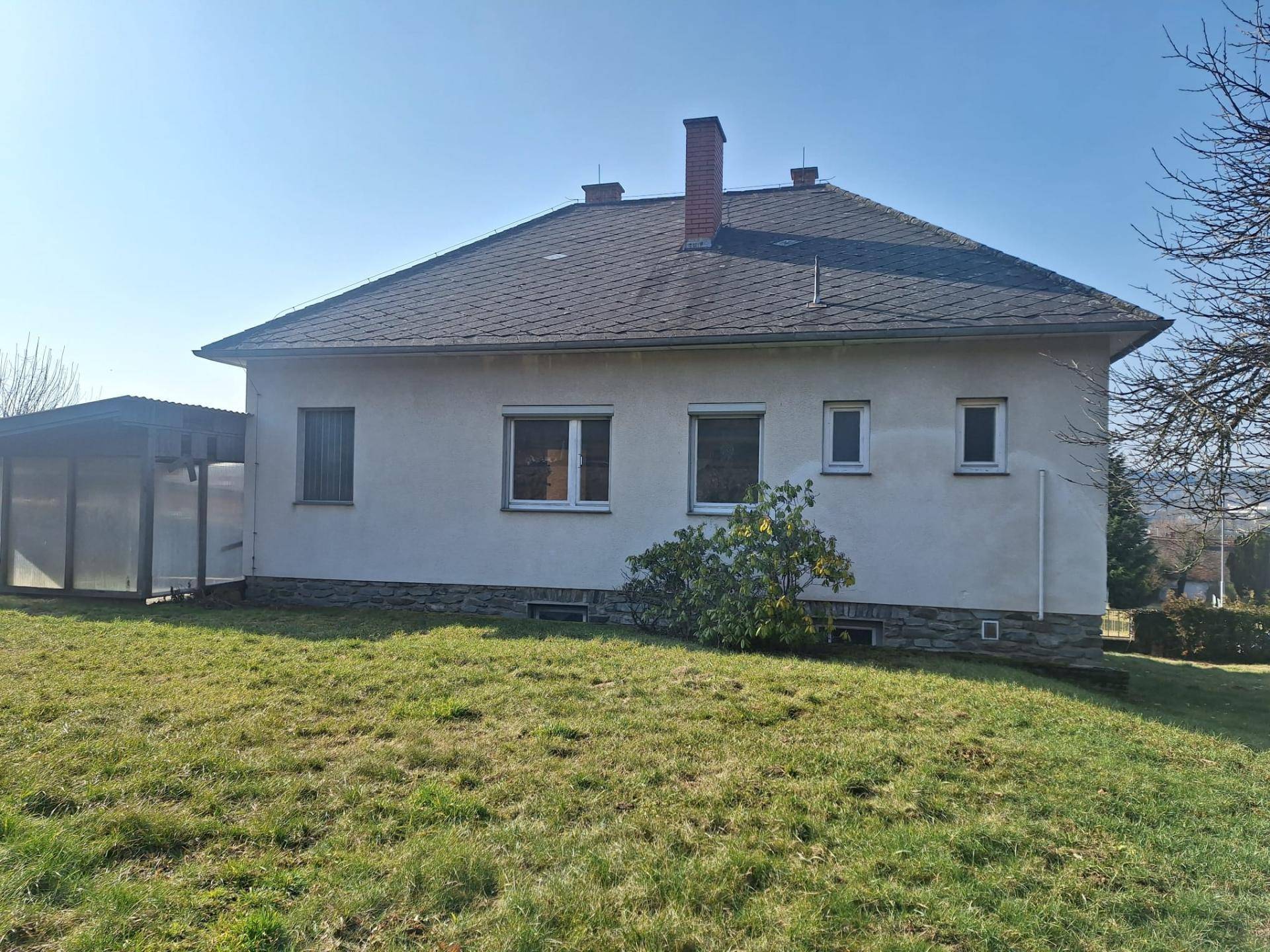 Rückansicht des Hauses mit großem Garten und überdachtem Bereich im Sonnenlicht.