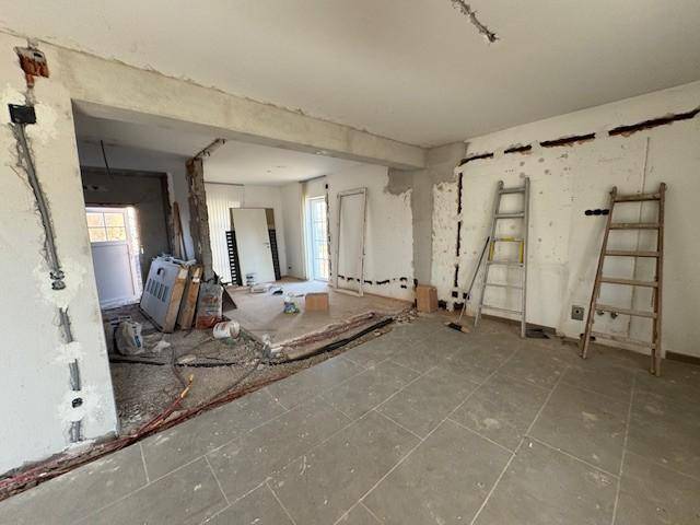 Offener Wohnbereich im Rohbau mit sichtbaren Leitungen und vorbereiteten Wänden.