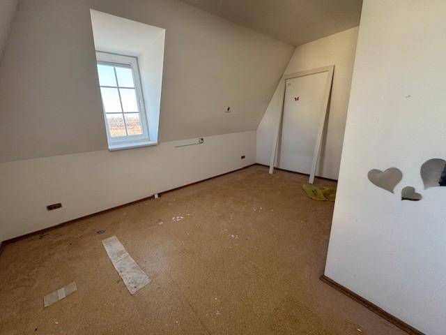 Leeres Zimmer im Dachgeschoss mit schrägen Wänden und Blick nach draußen.