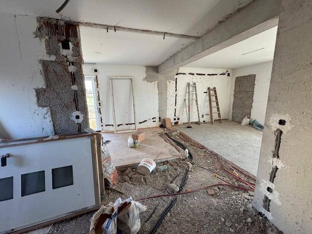 Großer Wohnbereich im Rohbau mit sichtbaren Installationen und viel Tageslicht.
