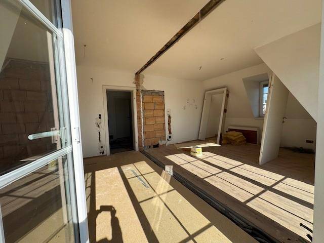 Offener Wohnbereich im Rohbau mit teilweise verlegtem Boden und viel Tageslicht.