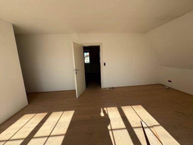 Helles Schlafzimmer im Dachgeschoss mit Holzboden und offener Tür zu einem weiteren Raum.