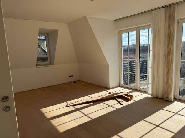 Lichtdurchflutetes Schlafzimmer im Dachgeschoss mit Holzboden, schrägen Wänden und großem Fenster.
