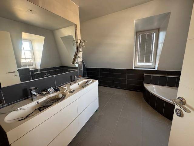 Modernes Badezimmer im Dachgeschoss mit Doppelwaschbecken, Badewanne und dunklen Fliesen.