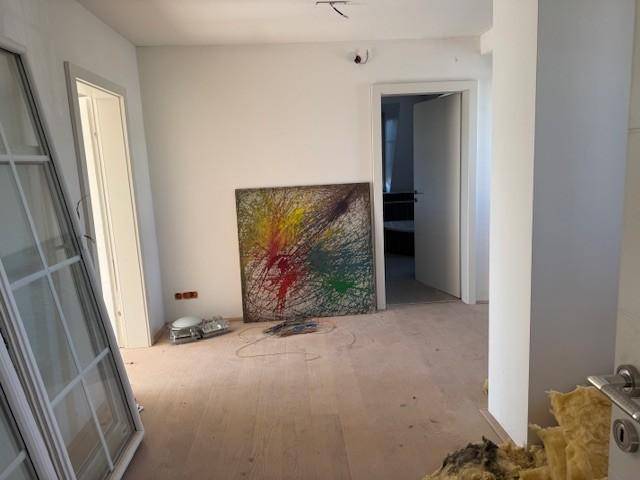 Innenraum im Rohbau mit einem farbenfrohen Kunstwerk und Blick in einen angrenzenden Raum.