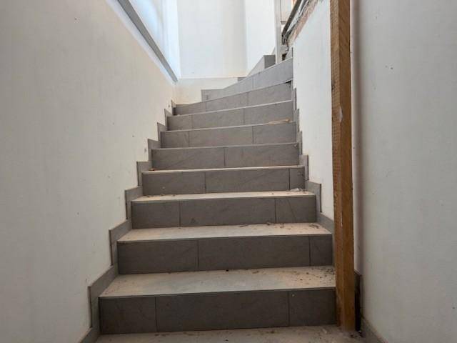 Geräumiger Treppenaufgang mit grauen Fliesenstufen und schlichten Wänden.