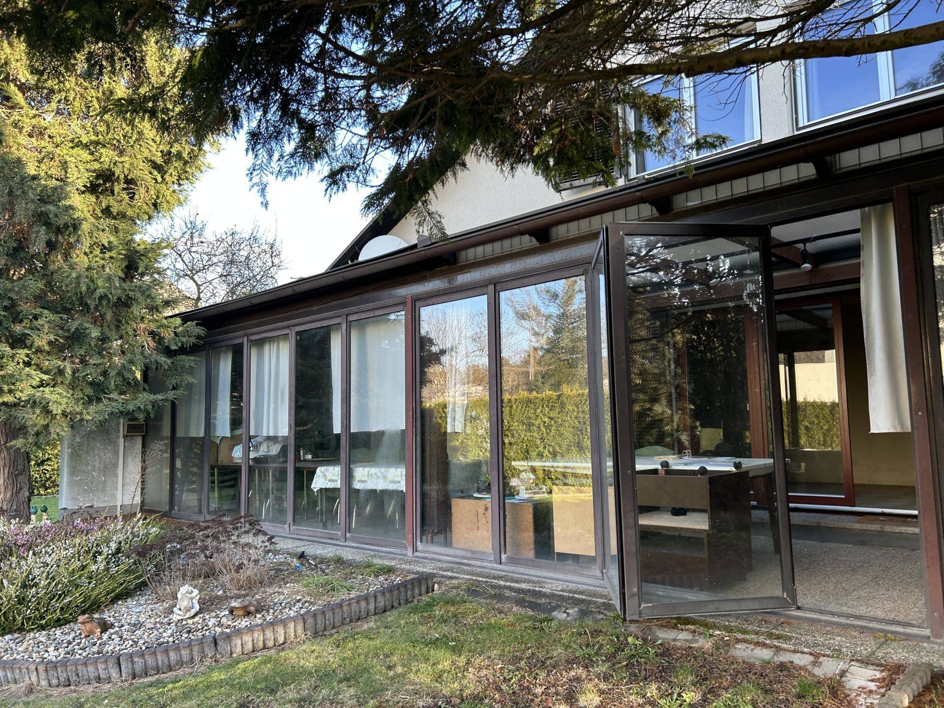 Heller Wintergarten mit großen Glasfronten und Zugang zum Garten, ideal für entspannte Stunden.