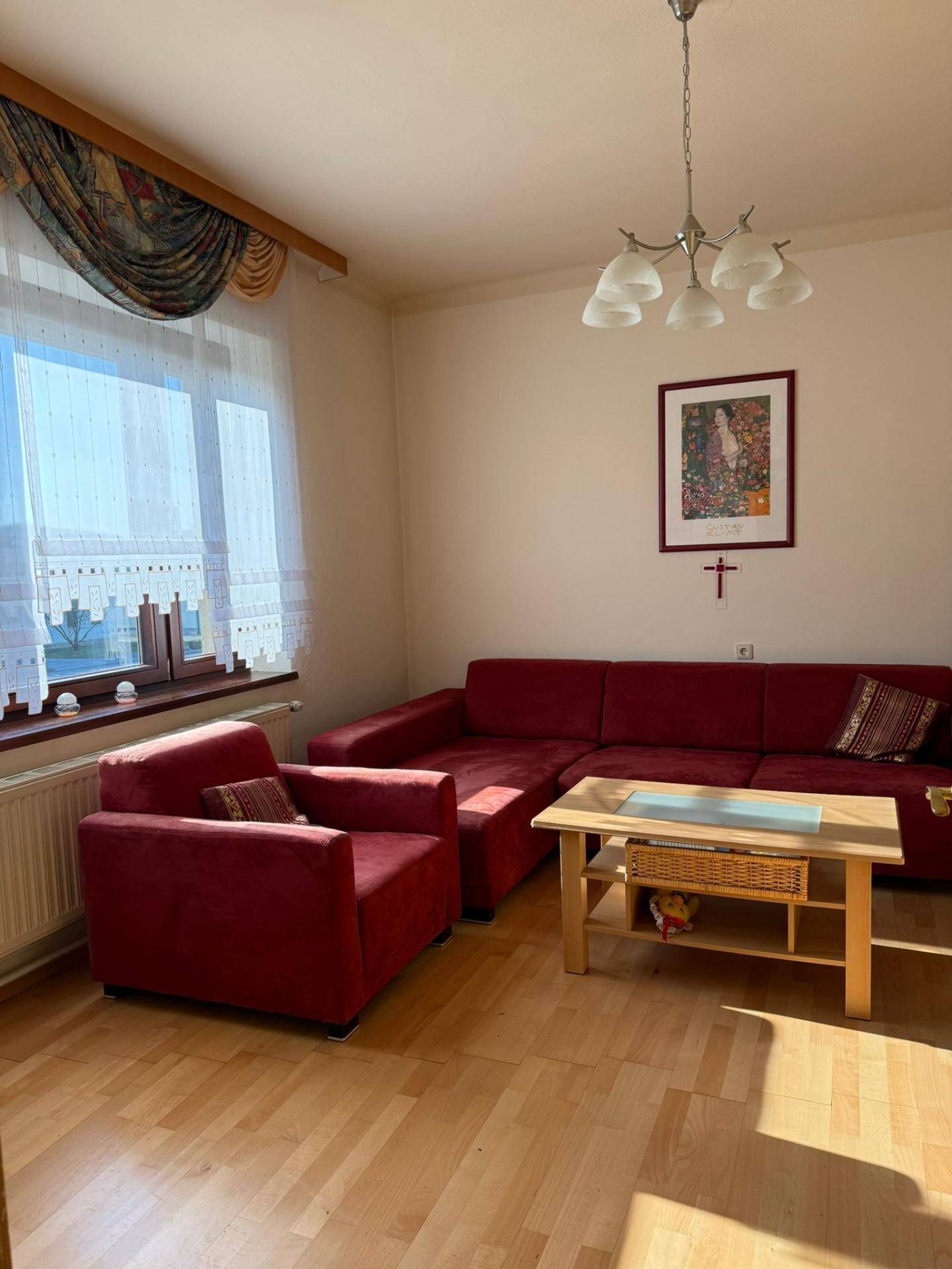 Gemütliches Wohnzimmer mit rotem Sofa, Holzboden und großem Fenster, sonnendurchflutet.