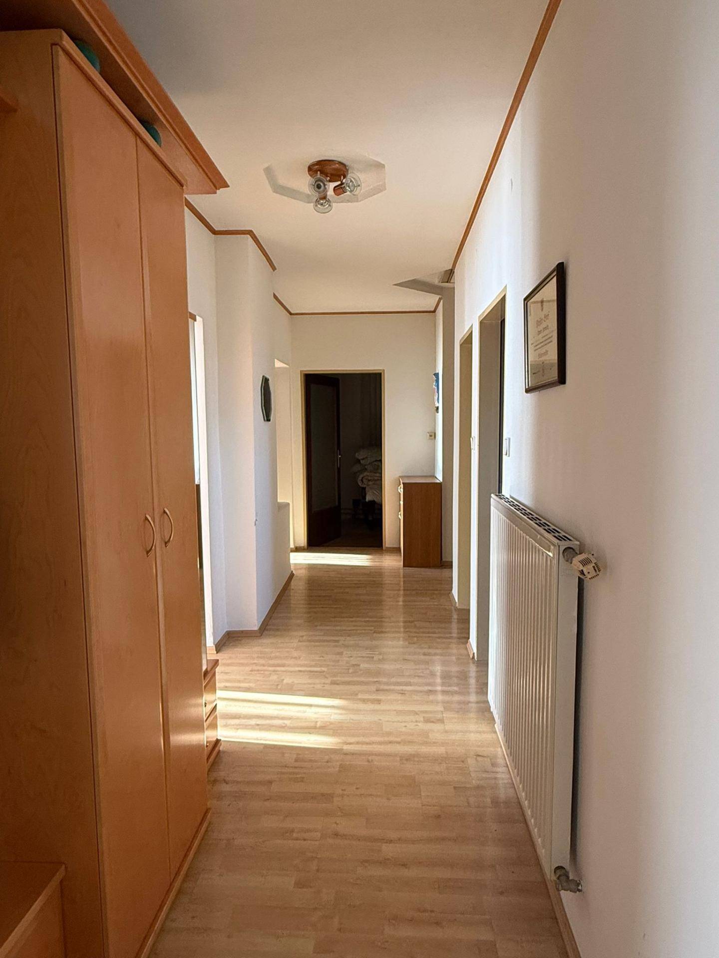 Heller Flur mit Laminatboden, Holzschrank und Heizkörper, sonnendurchflutet.
