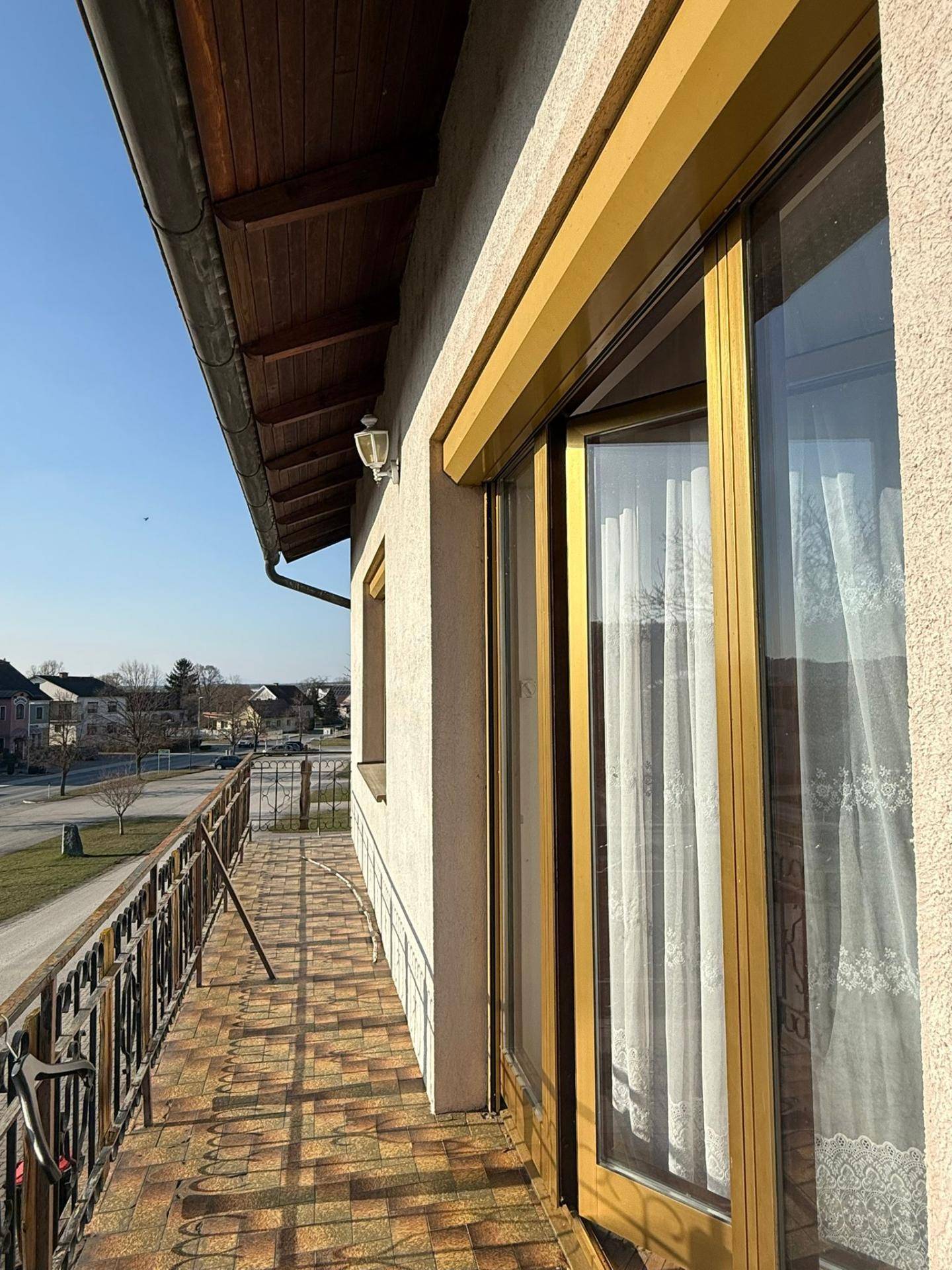 Langer Balkon mit Metallgeländer, gefliestem Boden und Blick auf die Umgebung.
