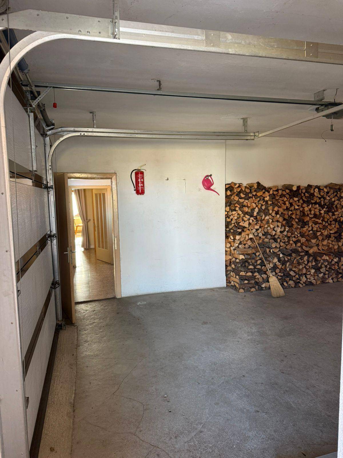 Geräumige Garage mit Betonboden, Holzlager und Zugang zu weiteren Räumen.