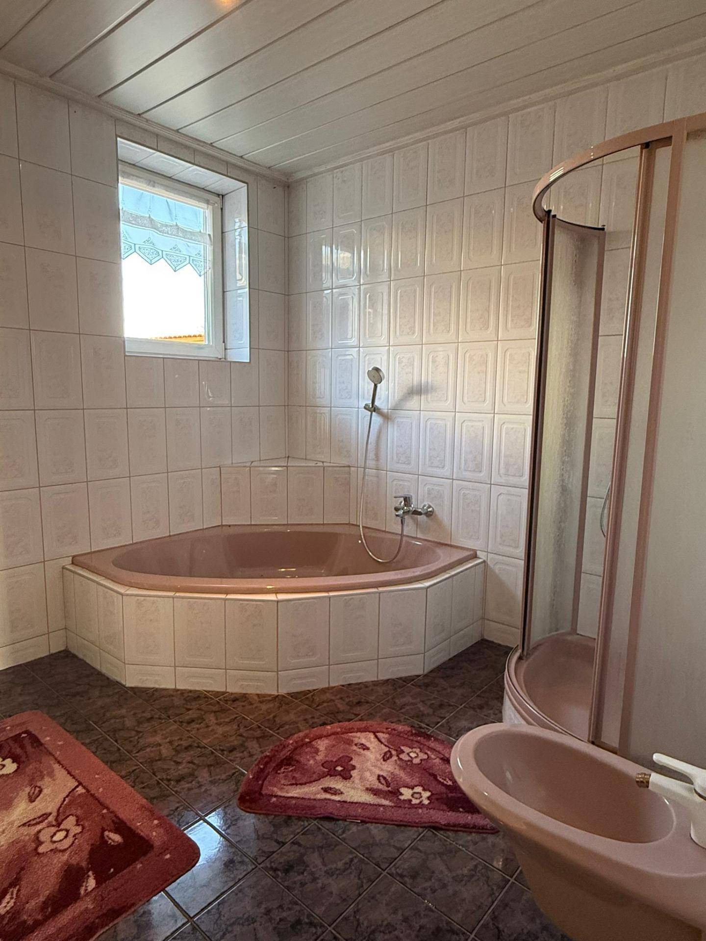 Badezimmer mit Eckbadewanne, Duschkabine und rosa Fliesen im 80er-Jahre-Stil.