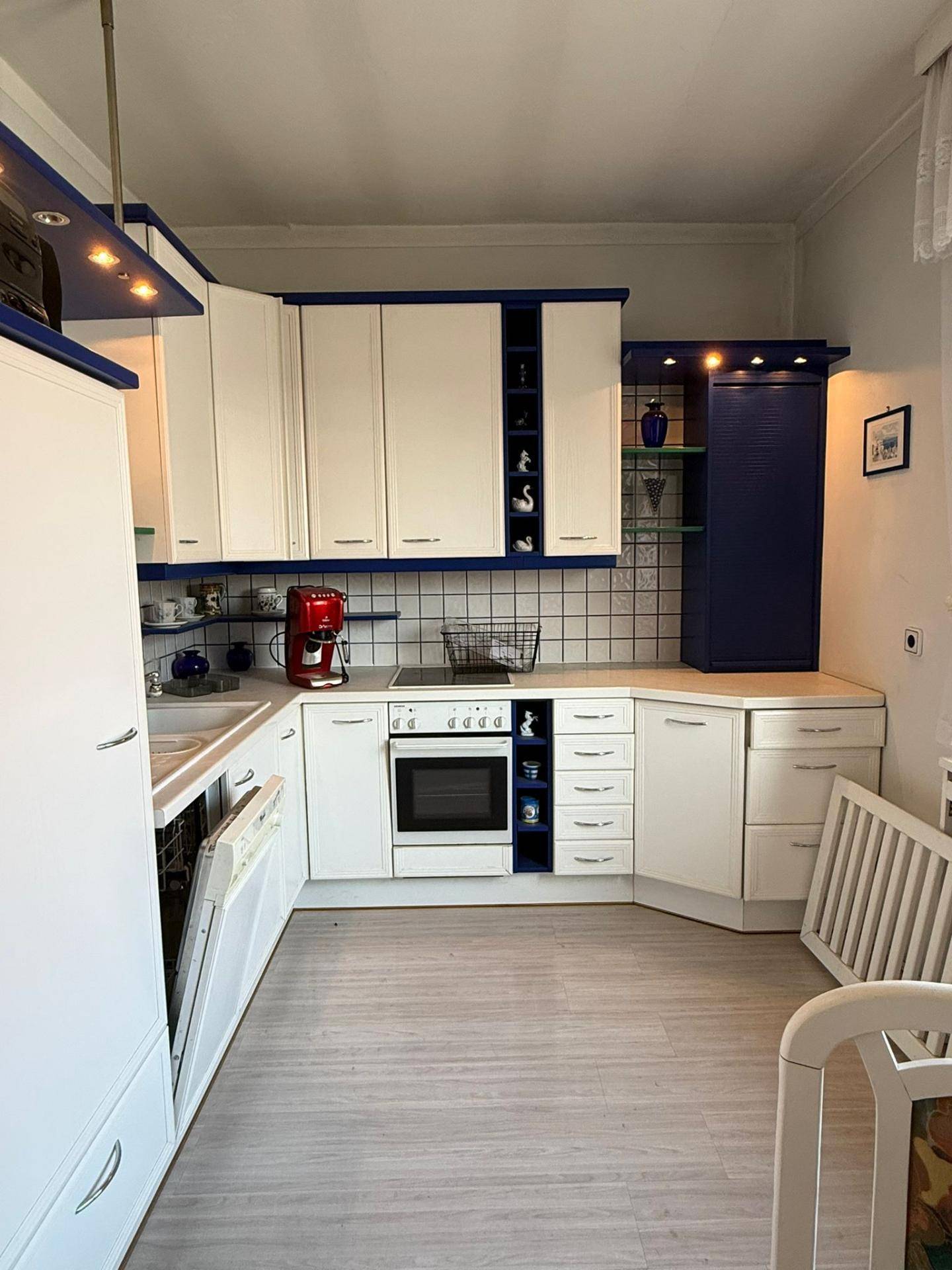 Moderne Küche mit weißen und blauen Schränken, integrierten Geräten und Essbereich.