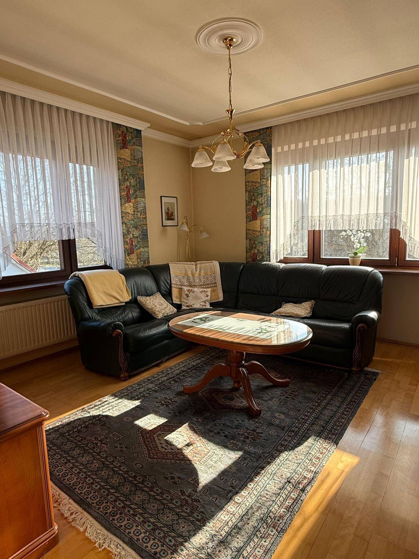 Geräumiges Wohnzimmer mit Ledersofa, Teppich und Stuckdecke, sonnendurchflutet.