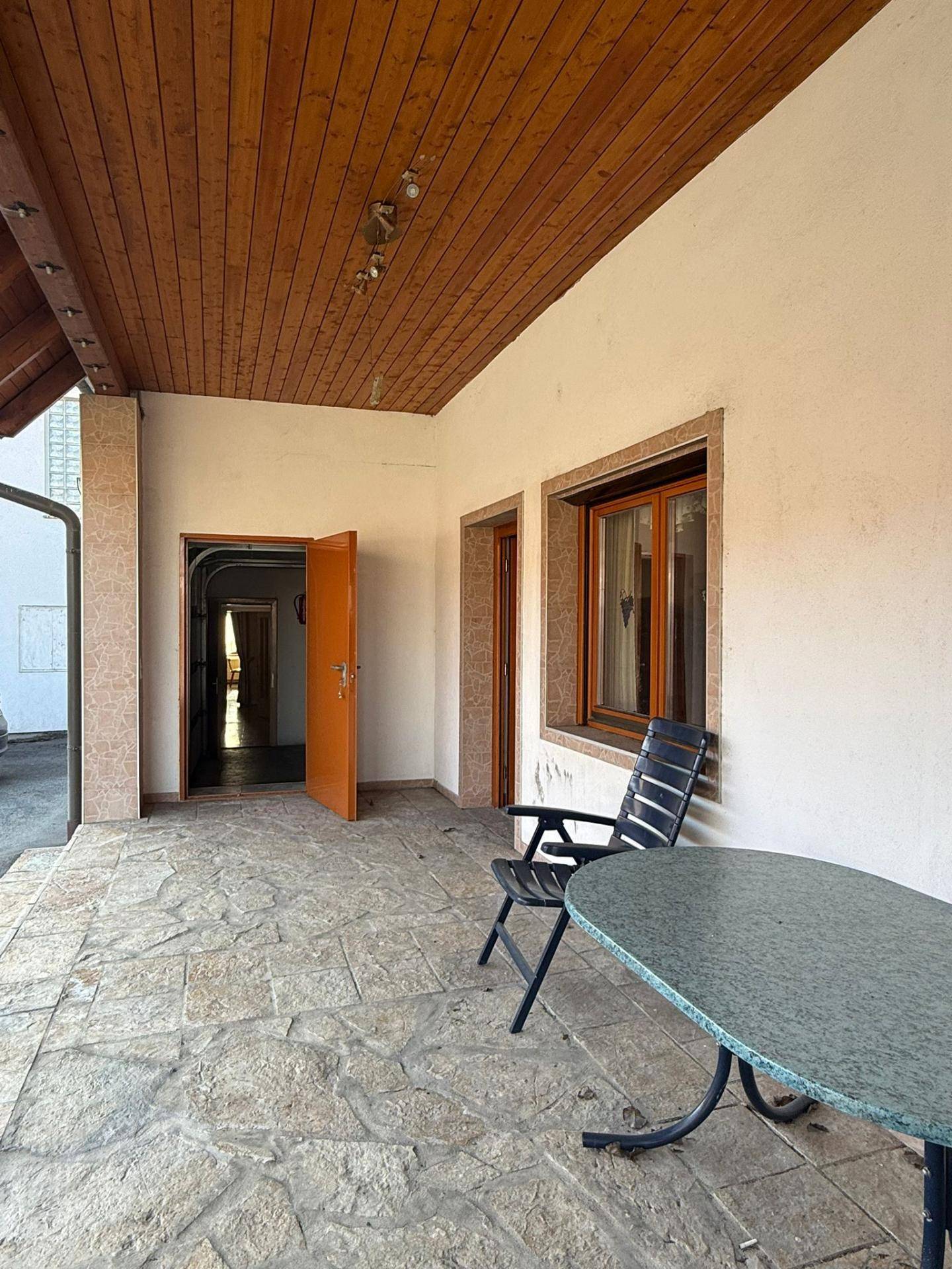 Überdachte Terrasse mit Steinfliesen, Sitzgelegenheiten und Holzbalkendecke.