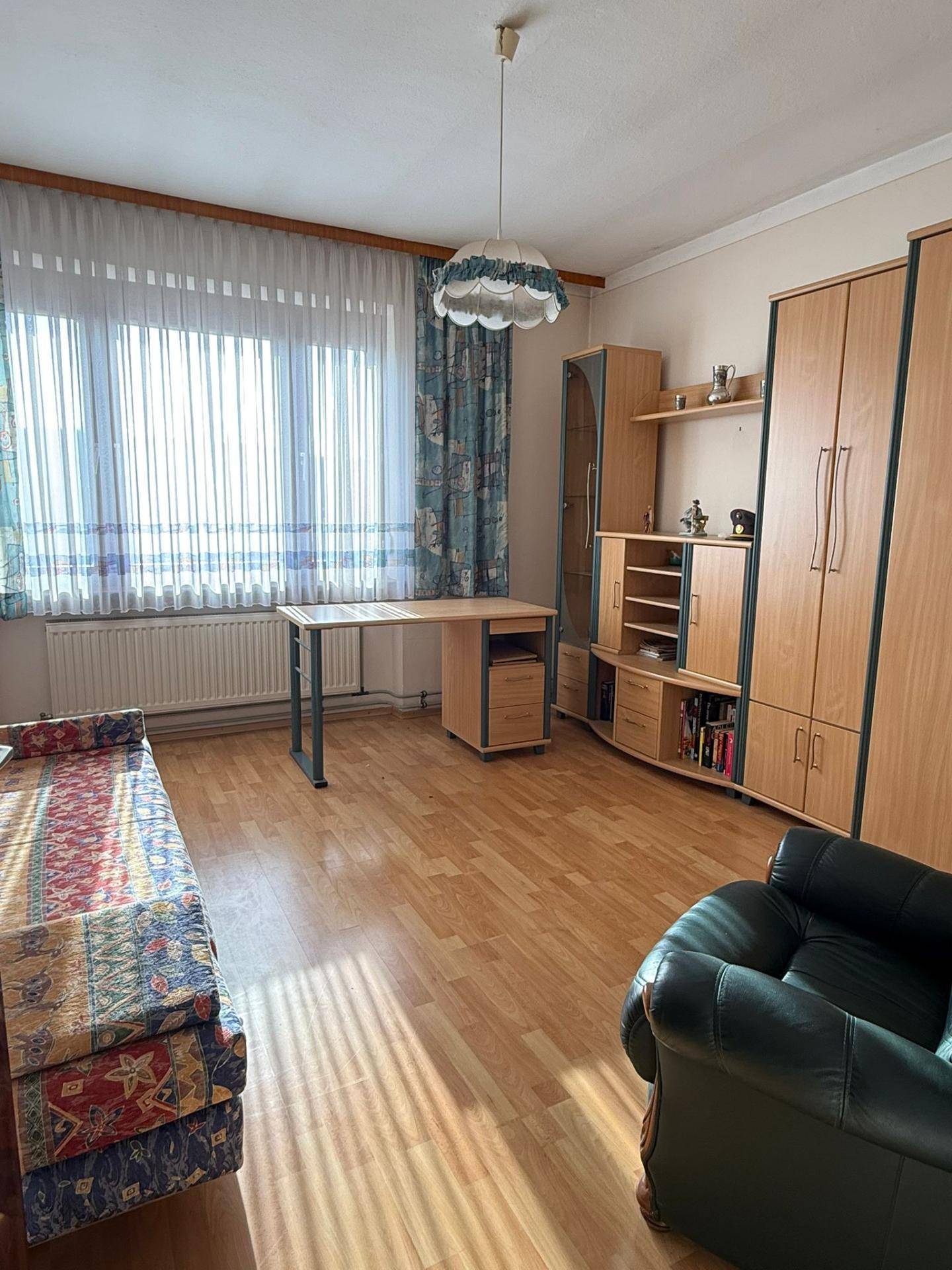 Helles Arbeitszimmer mit Holzmöbeln, Laminatboden und großem Fenster, gut beleuchtet.