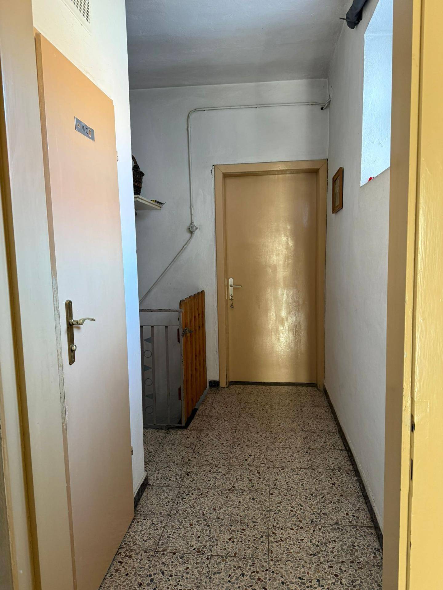 Schmaler Flur mit Terrazzoboden und mehreren Türen, einfacher Stil.