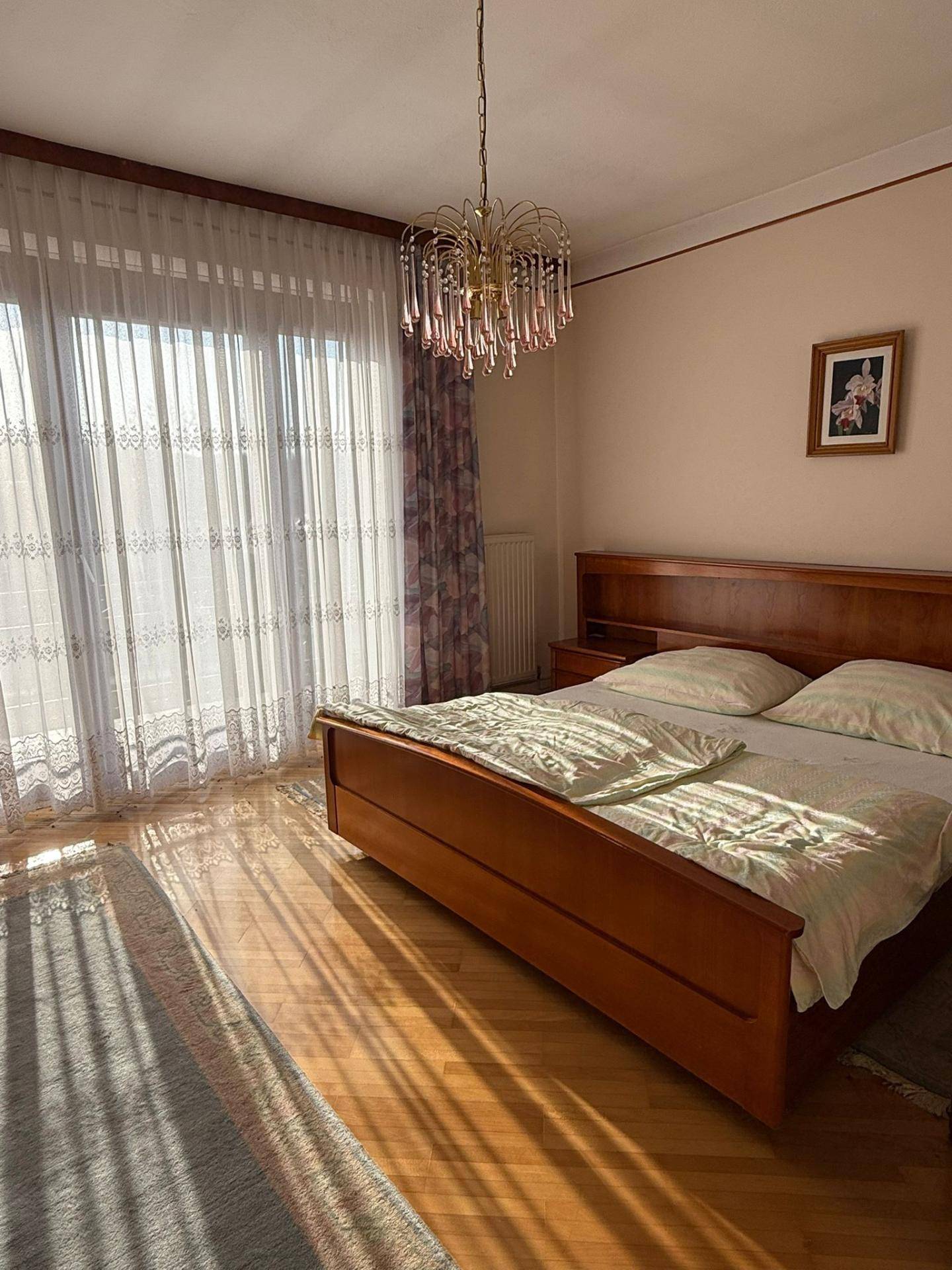 Helles Schlafzimmer mit Holzbett, Parkettboden und großem Fenster mit Balkonzugang.
