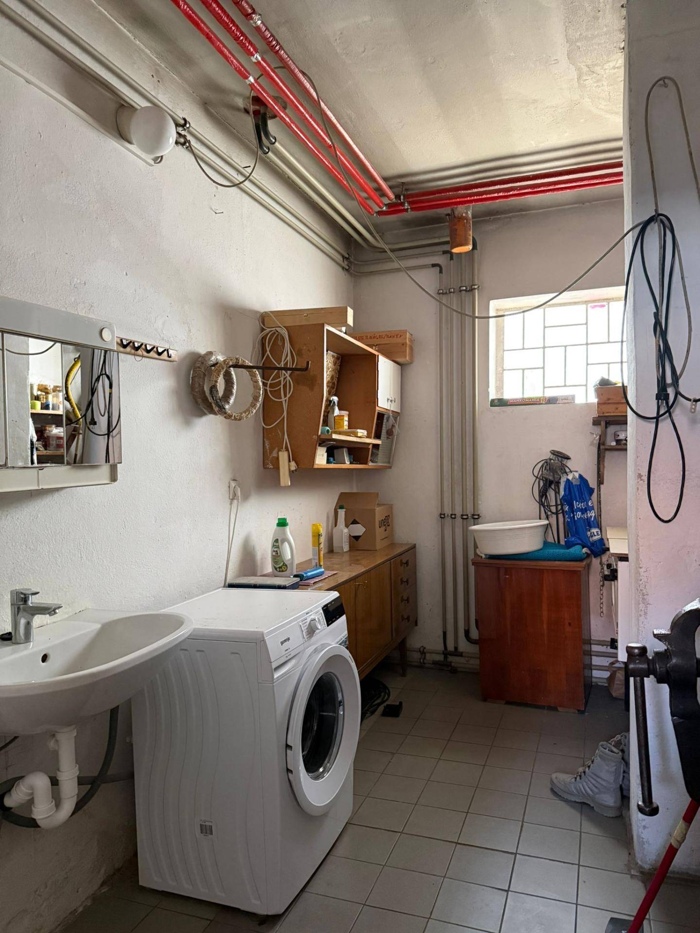 Praktischer Hauswirtschaftsraum mit Waschmaschine, Spülbecken und sichtbaren Leitungen.