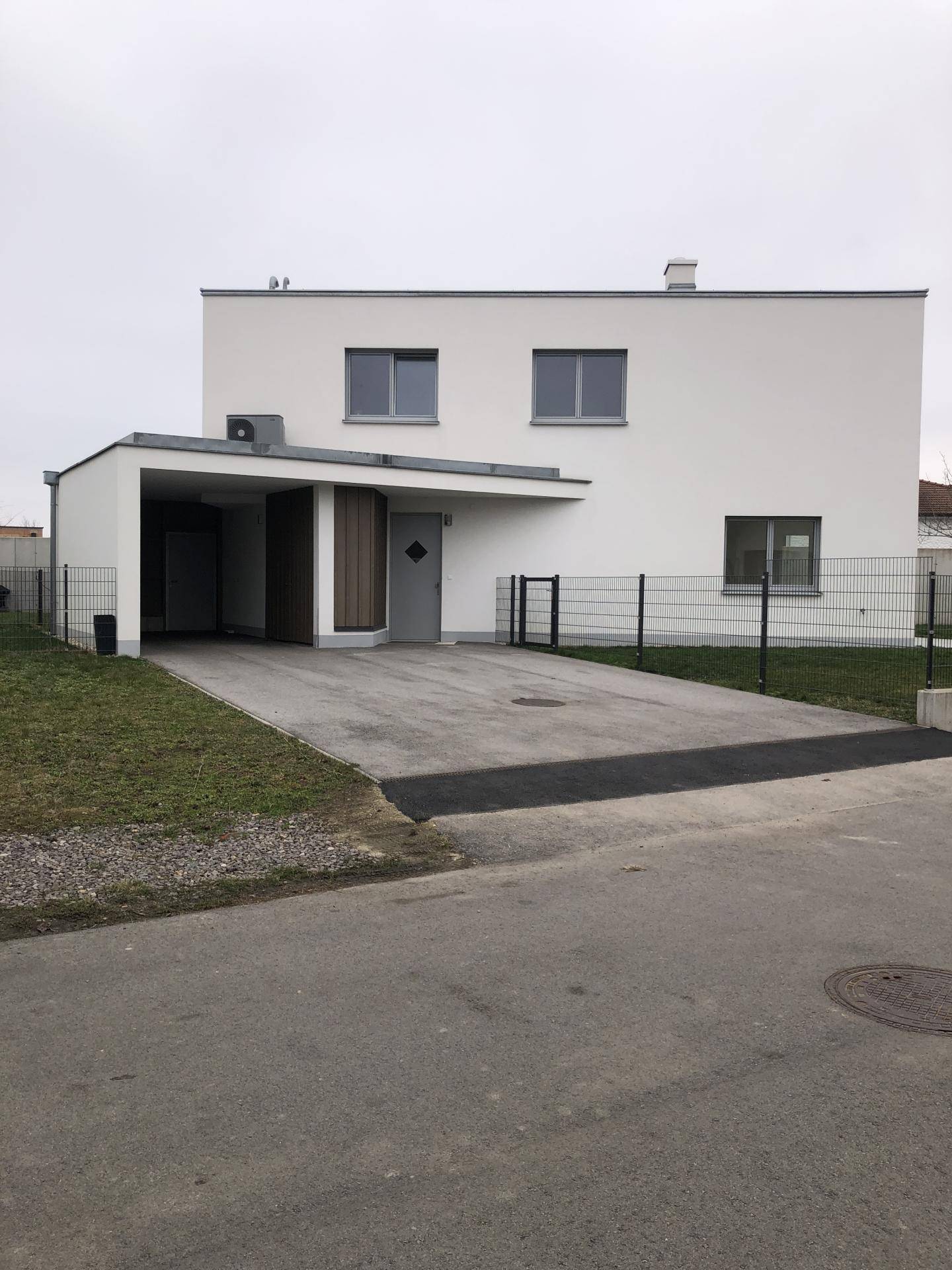 Vorderansicht des modernen Hauses mit Carport und Zufahrt auf einem gepflegten Grundstück.