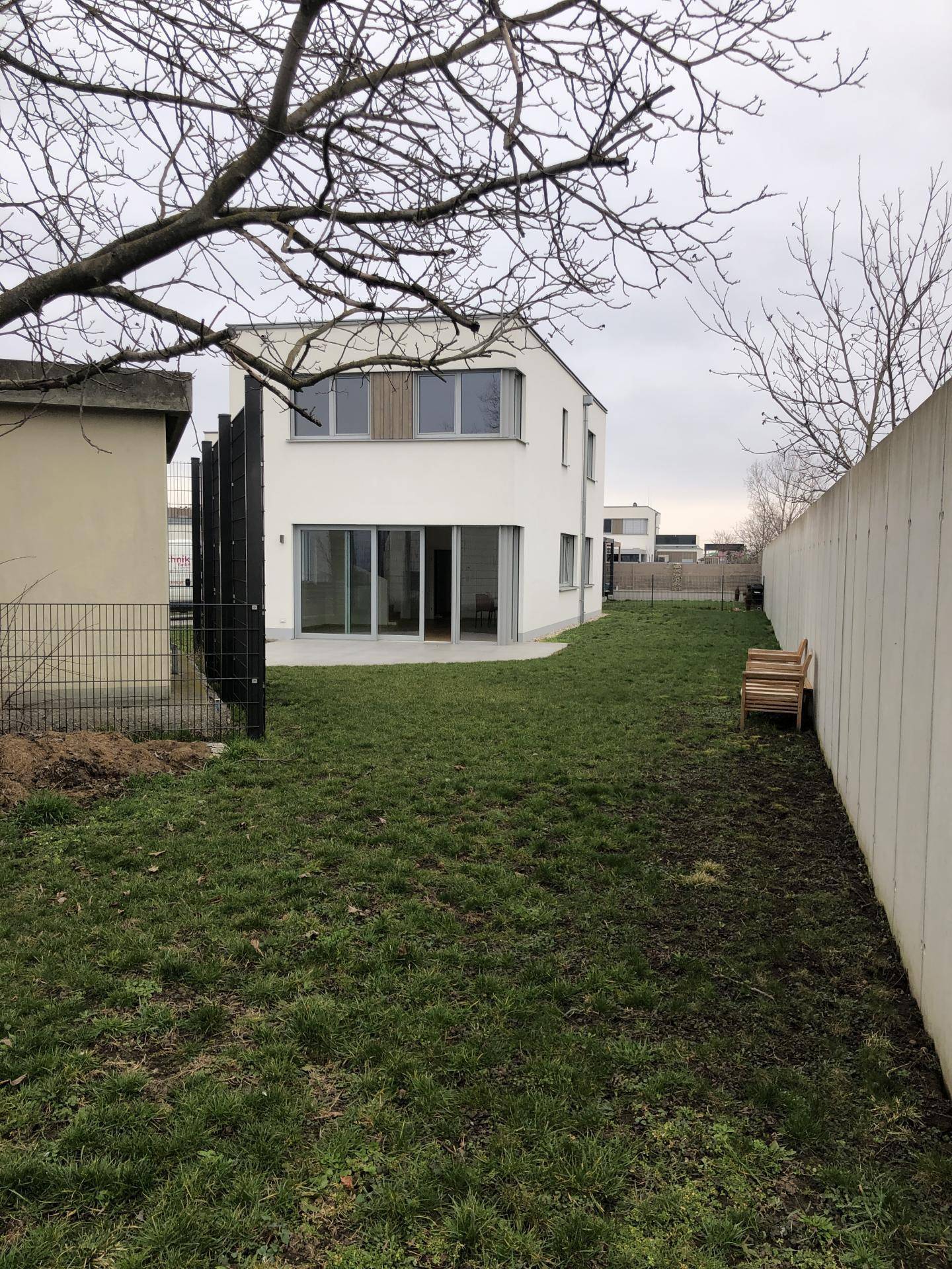 Hinterhof mit Rasenfläche, Terrasse und Blick auf die Rückseite des modernen Hauses.
