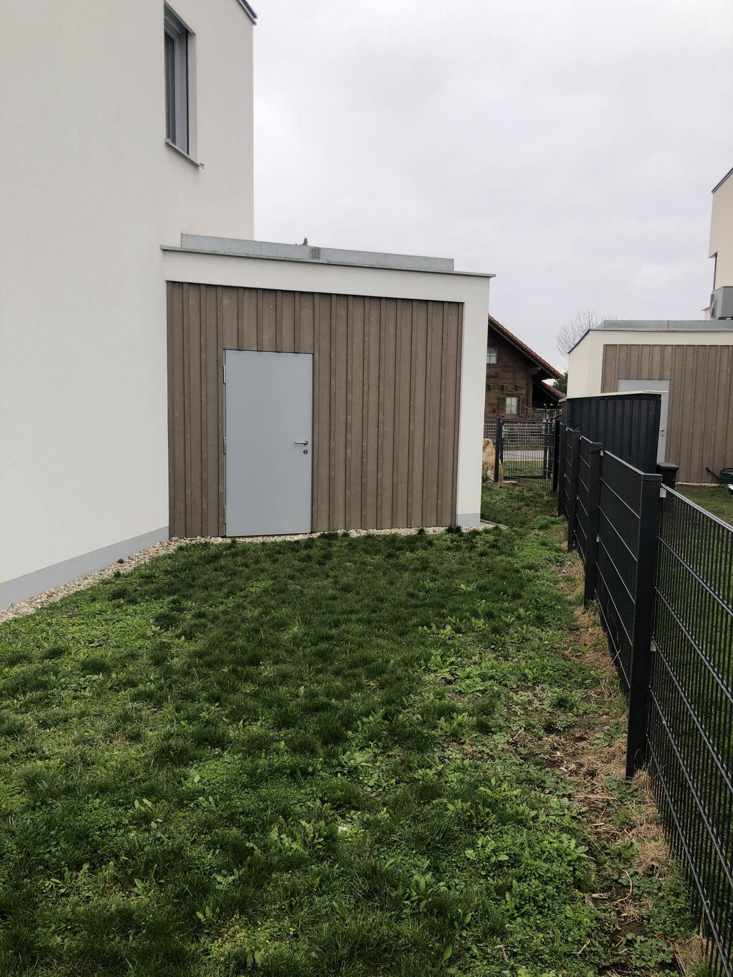 Seitenansicht des Hauses mit einem Holzschuppen und einem umzäunten Gartenbereich.