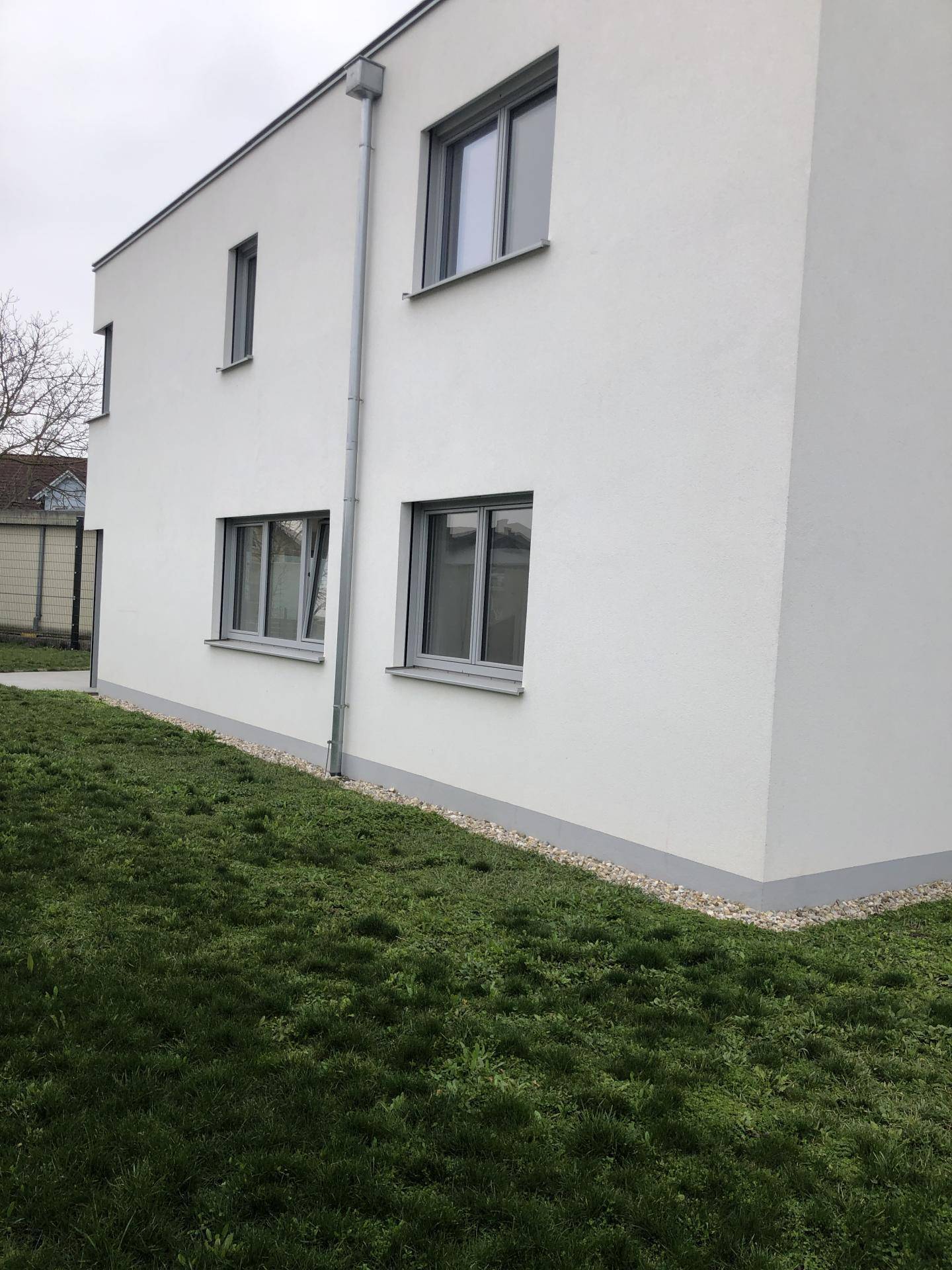Seitenansicht des modernen Hauses mit weißer Fassade, grauen Fenstern und Regenrinne.