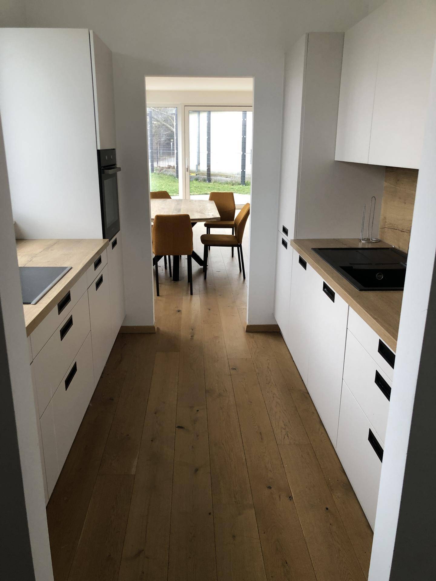 Moderne Küche mit weißen Schränken, Holzarbeitsplatten und Blick in den Essbereich.