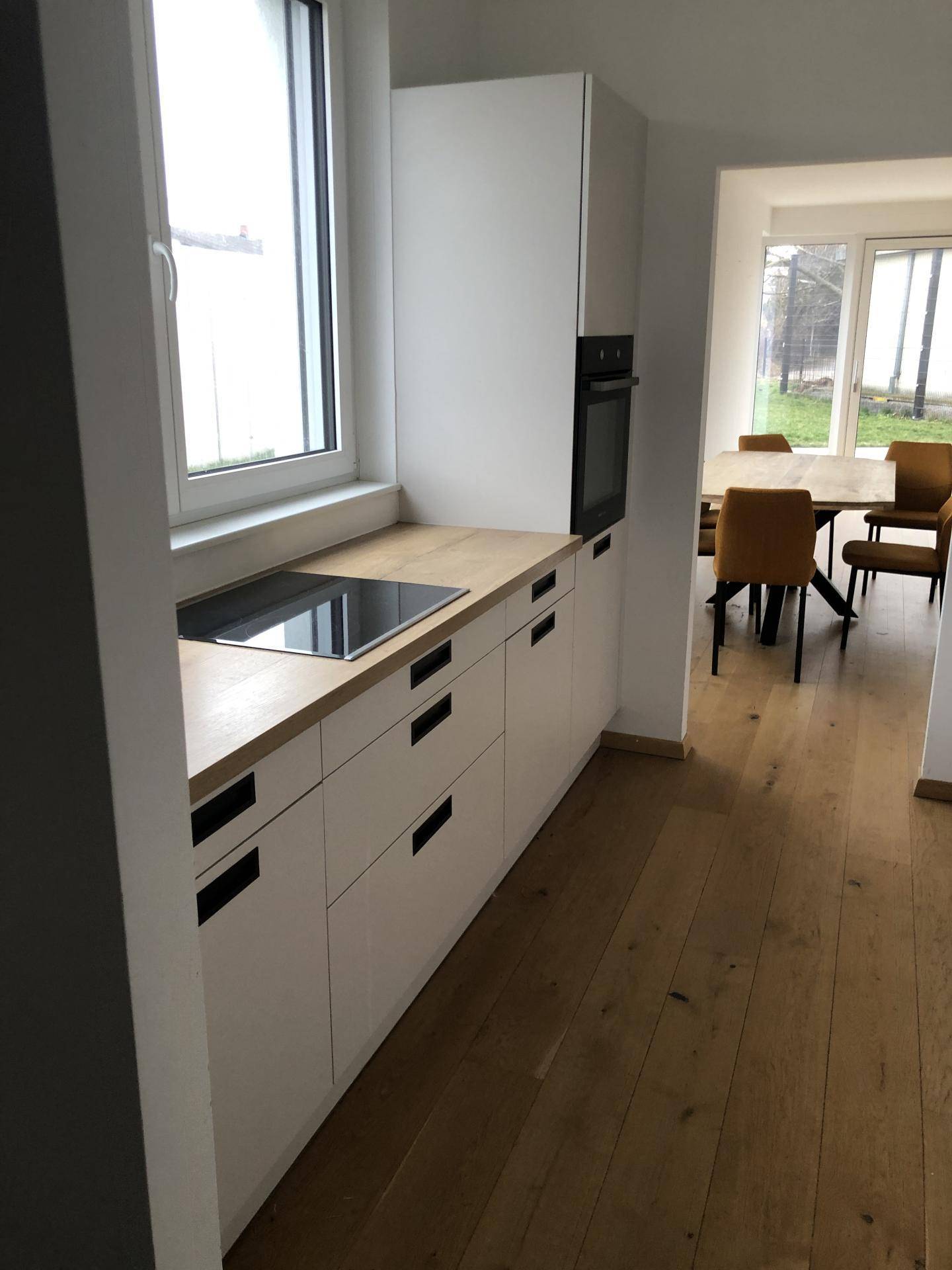 Helle Küche mit weißen Unterschränken, Holzarbeitsplatte und Fenster mit Blick ins Grüne.